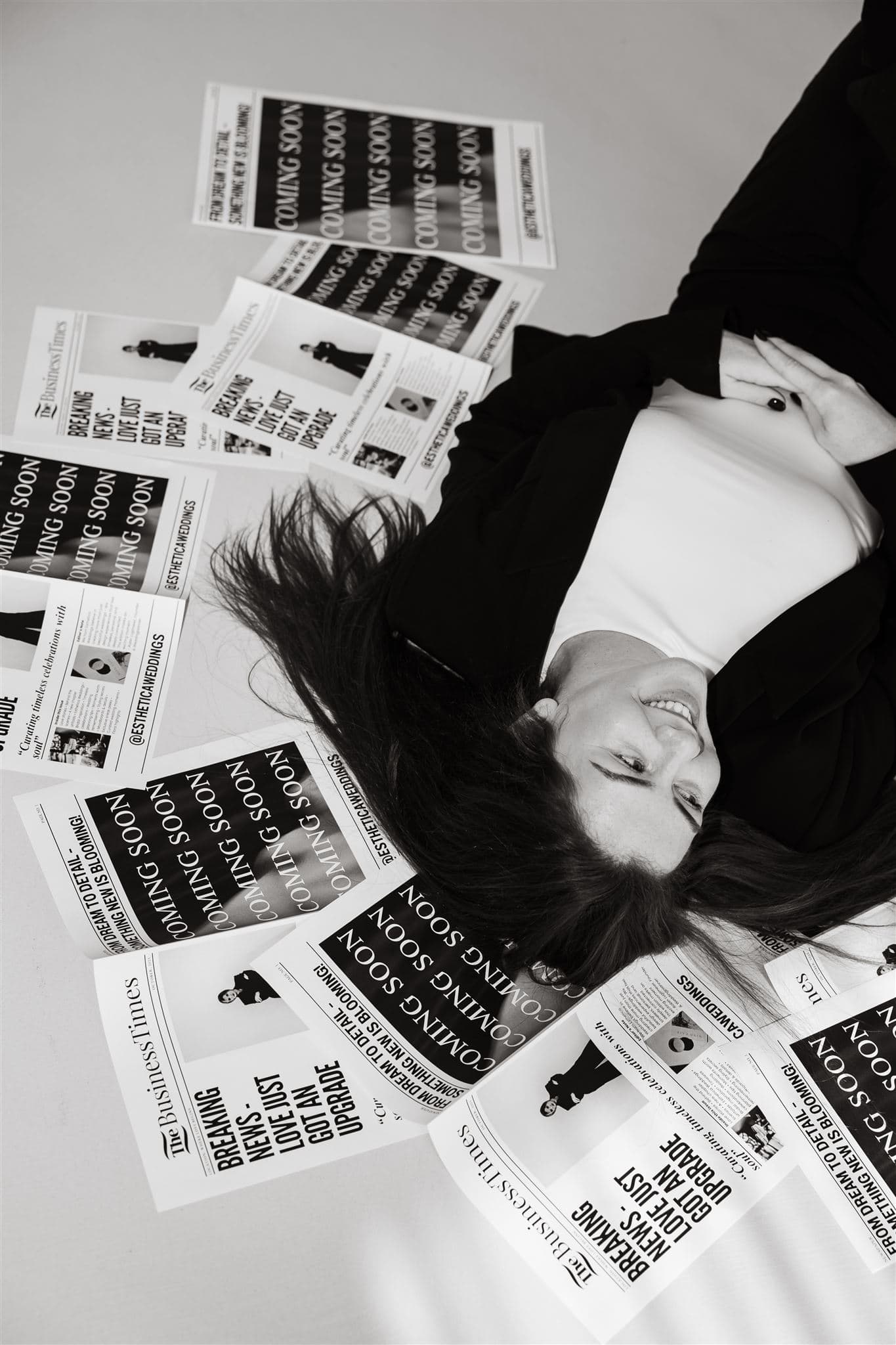 Vrouw liggend op de vloer, glimlachend tijdens een branding shoot, omringd door "COMING SOON" flyers voor "The Business Institute.