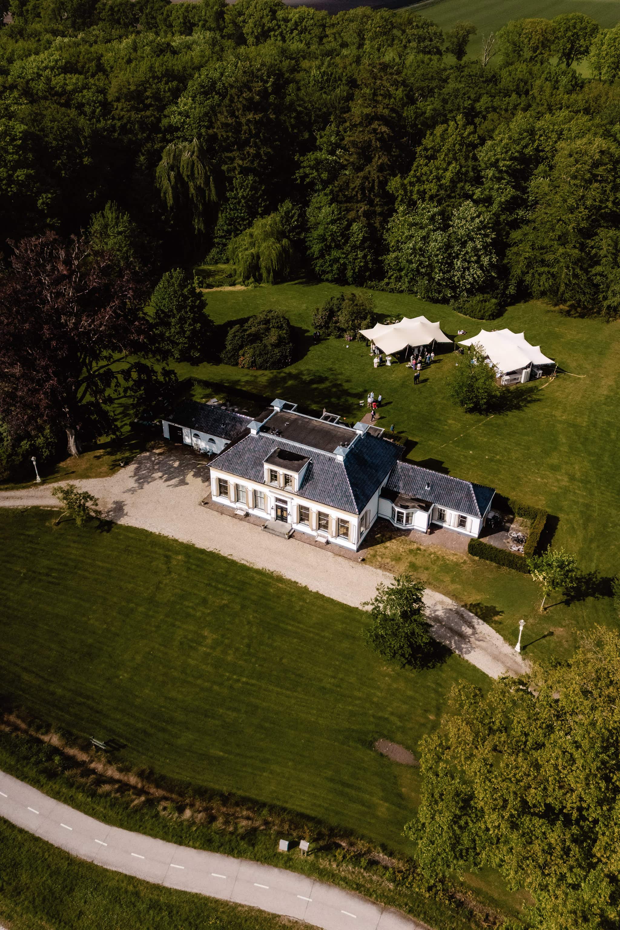 Dronefoto van trouwlocatie Klein Soestdijk in Veenhuizen, omringd door groene gazons, bomen en witte tenten.