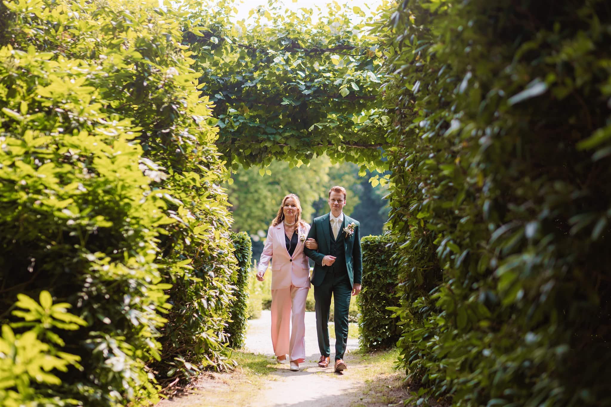 Trouwfoto van de bruidegom die met zijn moeder naar de ceremonie in het bos van Landgoed Lemferdinge loopt.