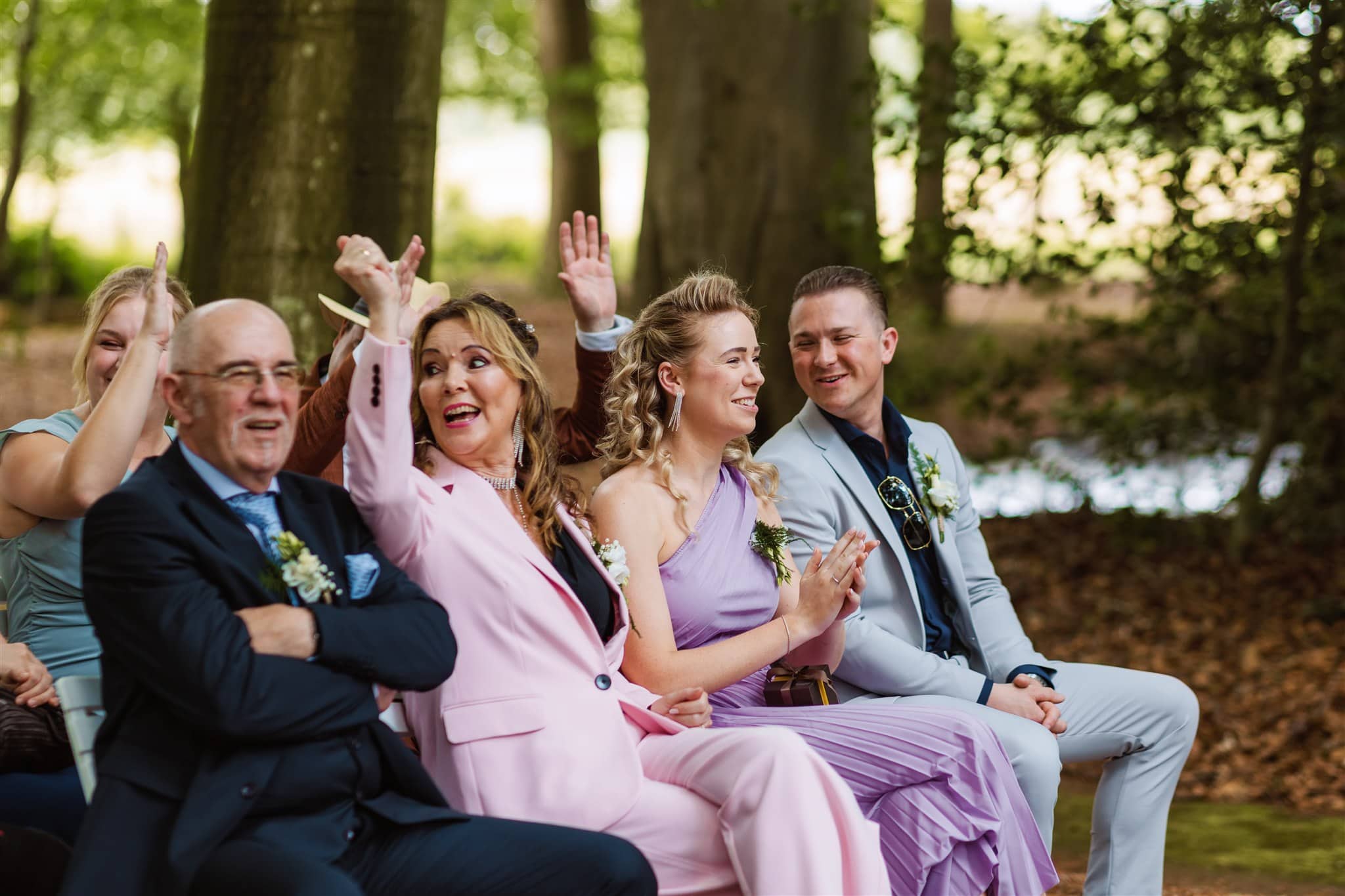 Bruiloftsgasten glimlachen en juichen tijdens een trouwceremonie in het bos van Landgoed Lemferdinge in Drenthe.