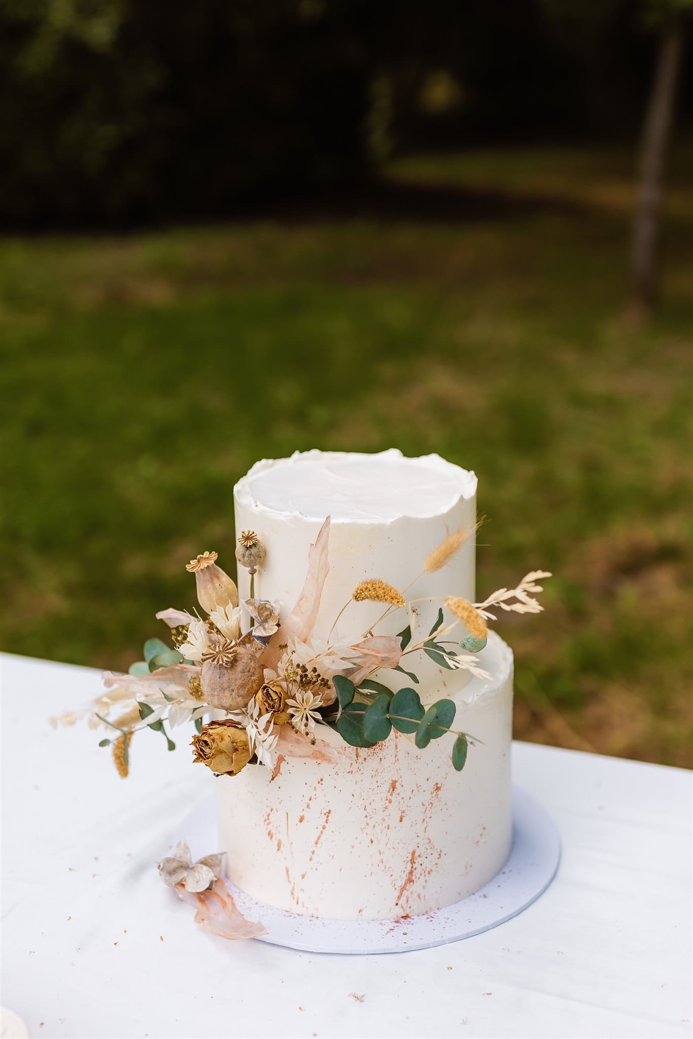 In de tuin van de trouwlocatie in Drenthe Landgoed Lemferdinge staat een witte taart met twee lagen, versierd met gedroogde bloemen.