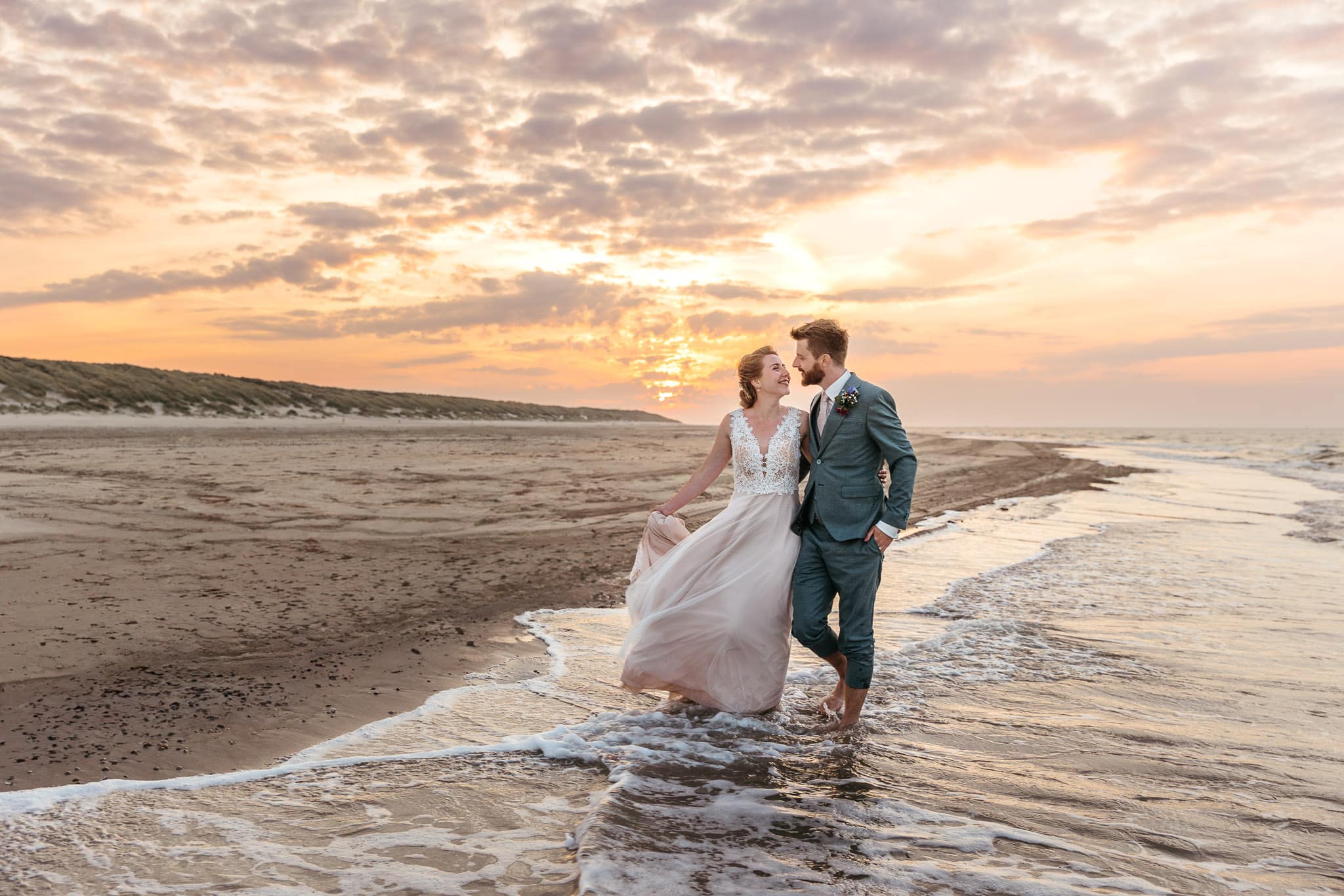 Een bruid en bruidegom staan bij zonsondergang op het strand op Vlieland, vastgelegd door een getalenteerde trouwfotograaf in Friesland.