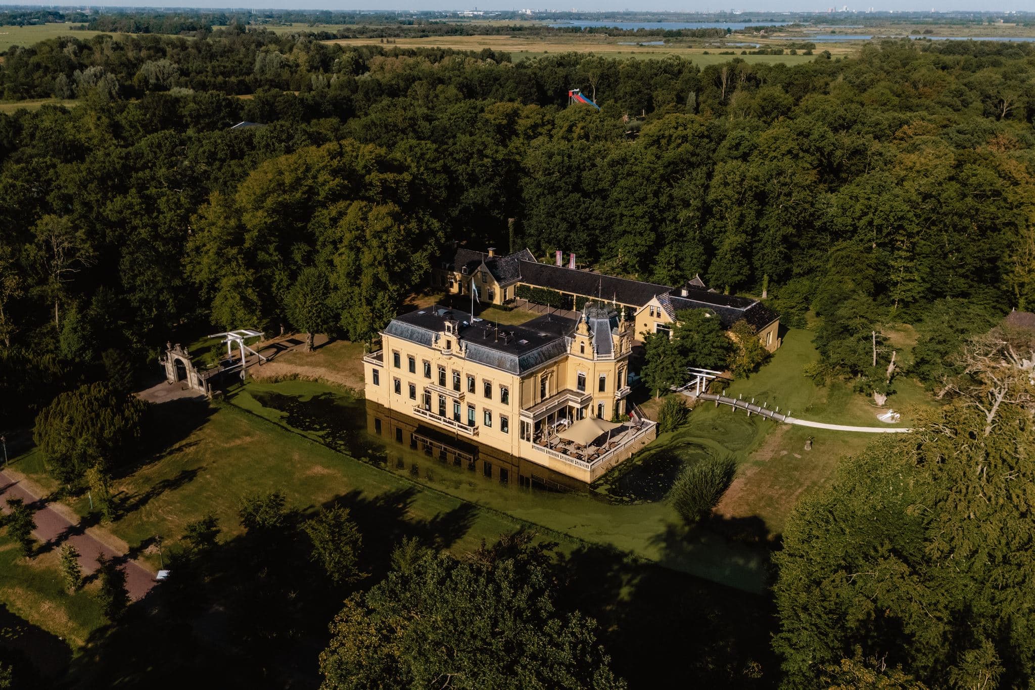 Drone foto van de trouwlocatie Borg Nienoord, een geel gebouw gelegen tussen de bossen in Leek.