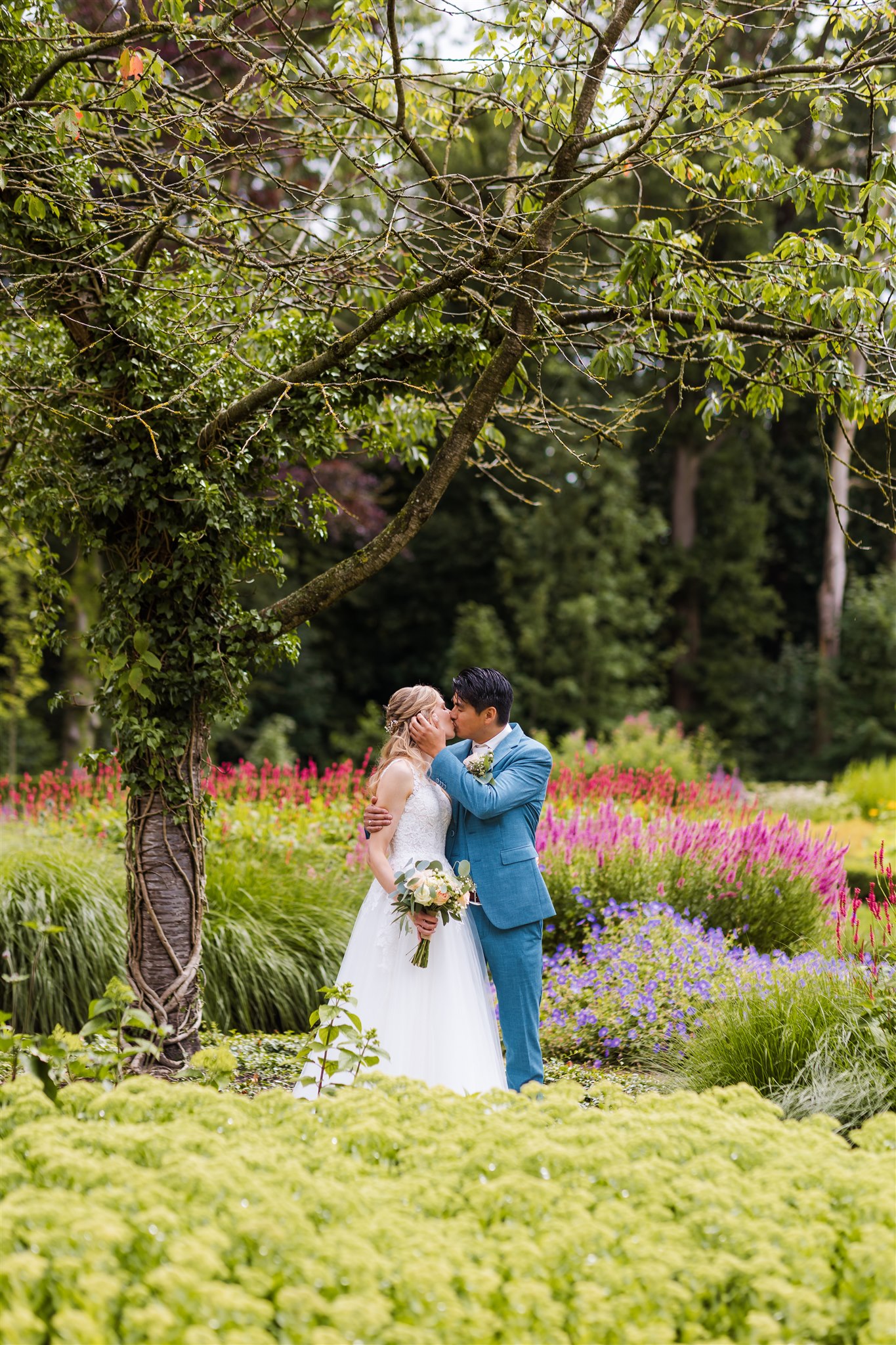 Bruidspaar kust elkaar in de bloeiende Engelse tuin tijdens de fotoshoot op hun bruiloft bij Borg Nienoord
