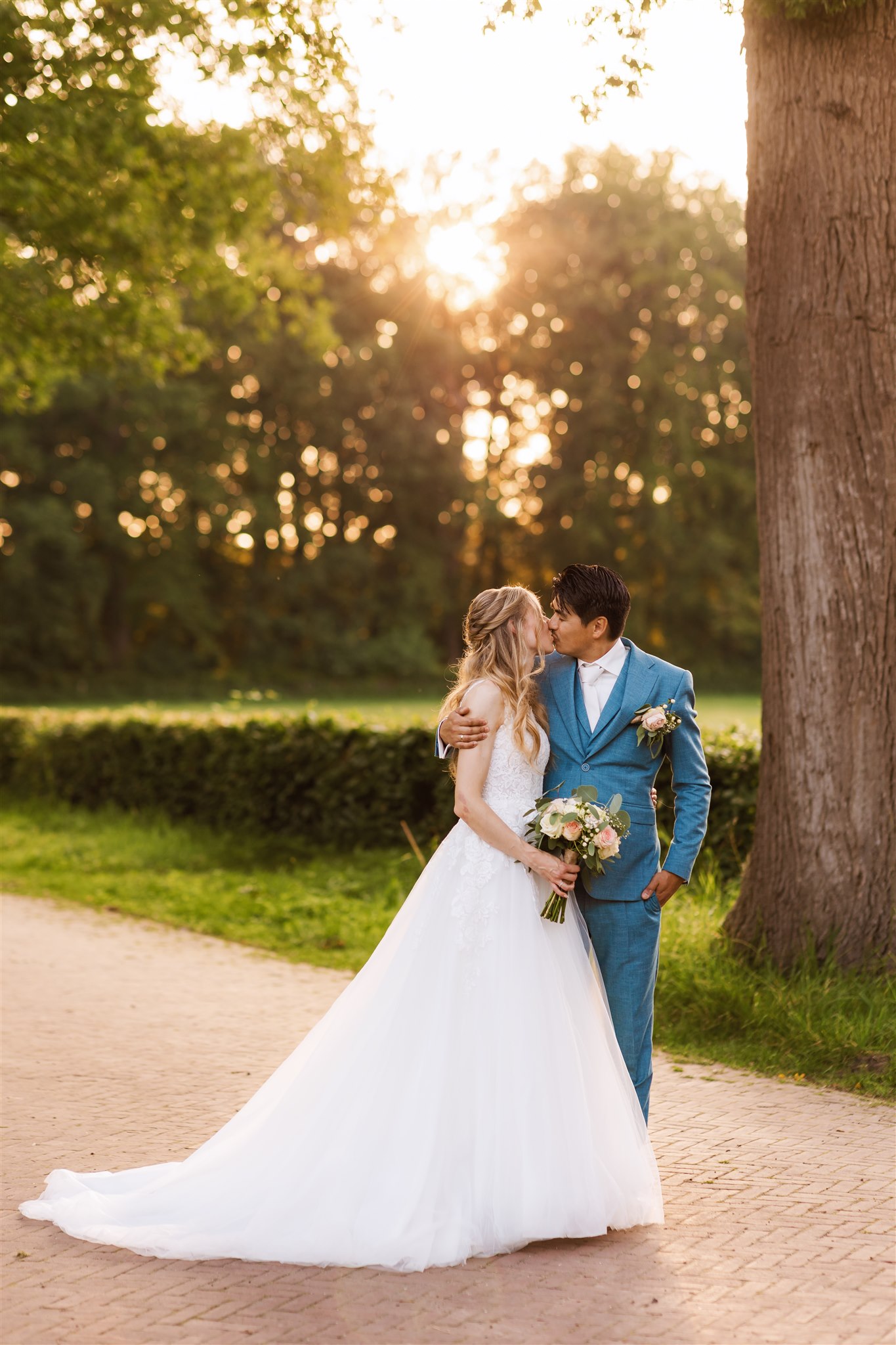 Bruidspaar kust elkaar tijdens hun fotoshoot op de boslaan met zonsondergang op hun bruiloft bij Borg Nienoord