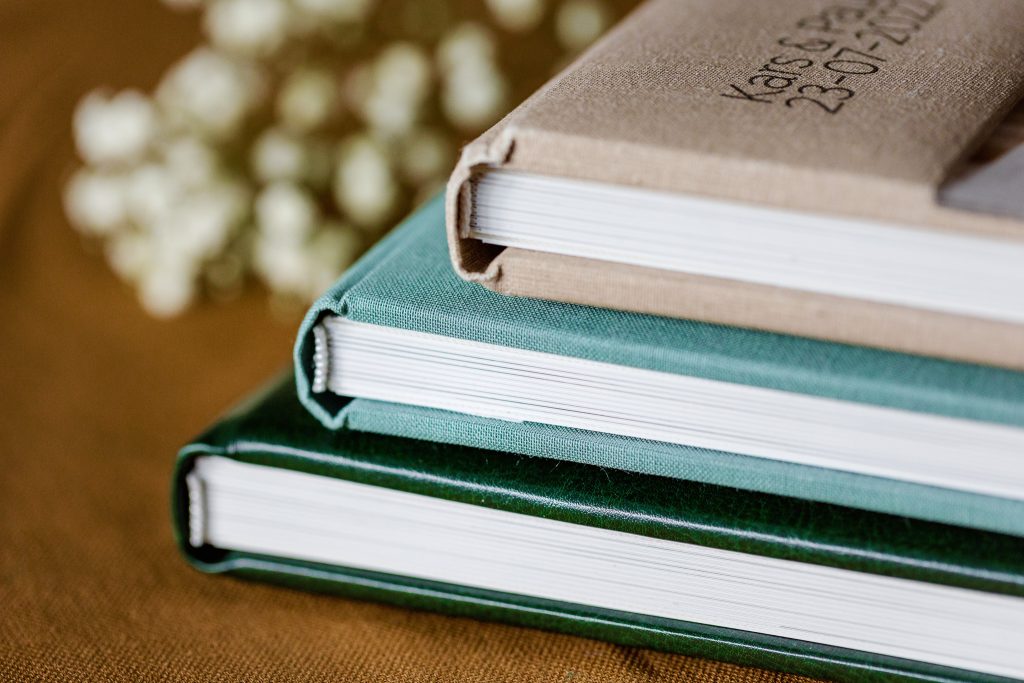 Een stapel hardcoverboeken met de nadruk op de rug van het bovenste boek, tegen een achtergrond met trouwfoto's.