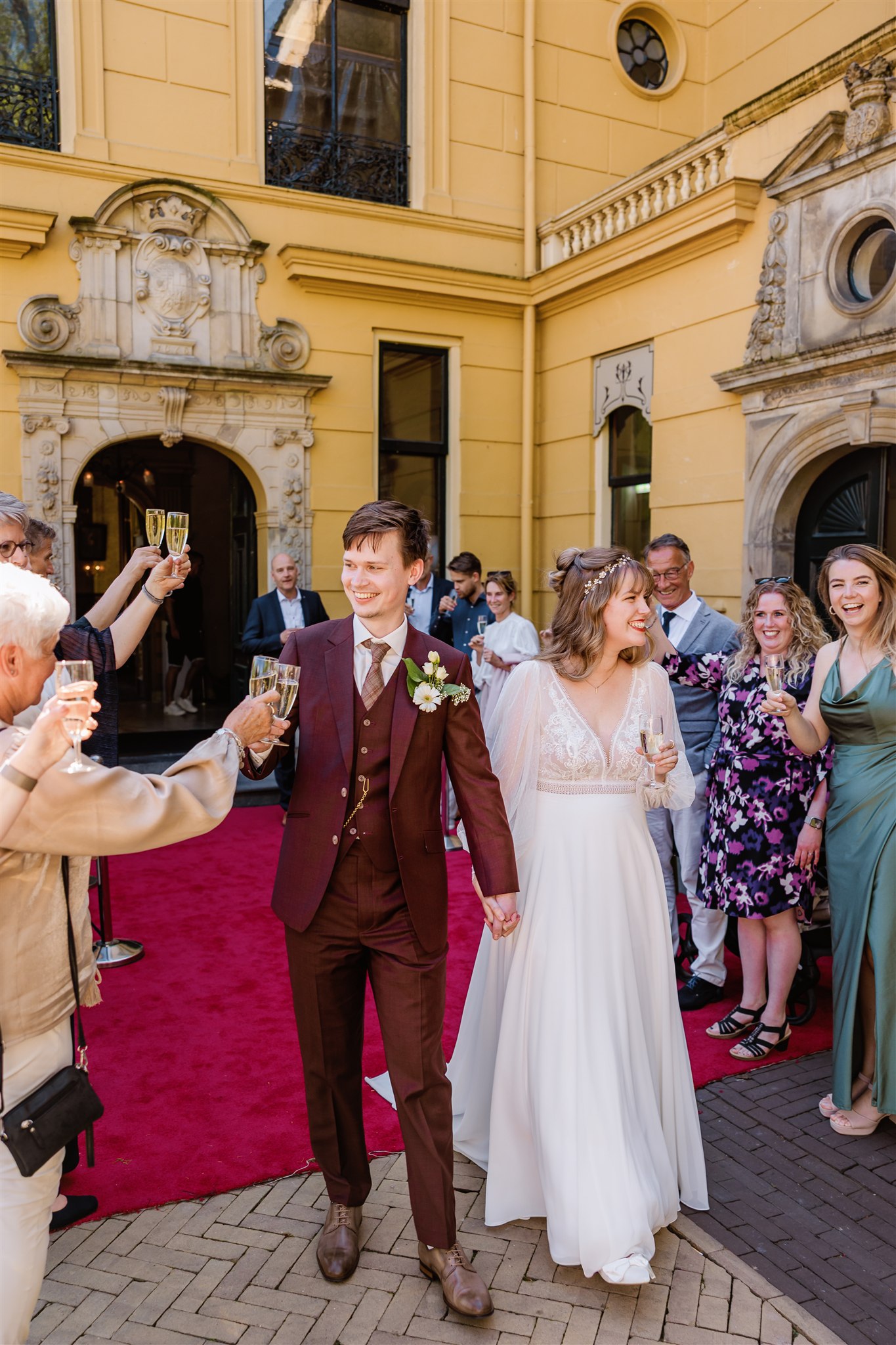 Bruidspaar loopt lachend met champagne door een erehaag bij de ingang van Borg Nienoord na hun trouwceremonie