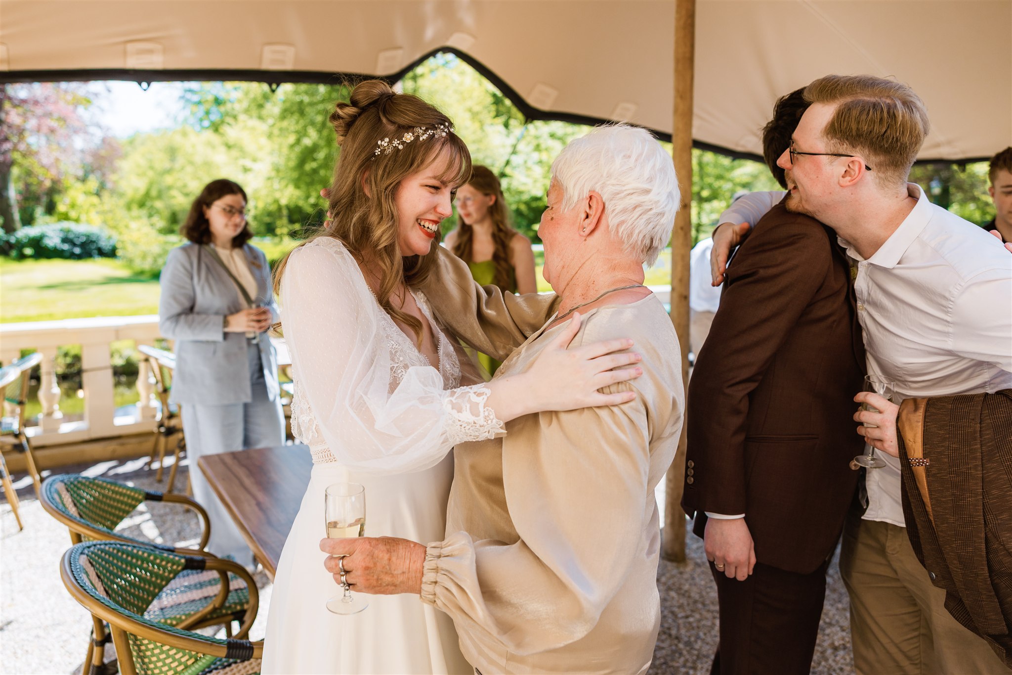 Een bruid in een witte jurk glimlacht en omhelst haar oma op het terras.