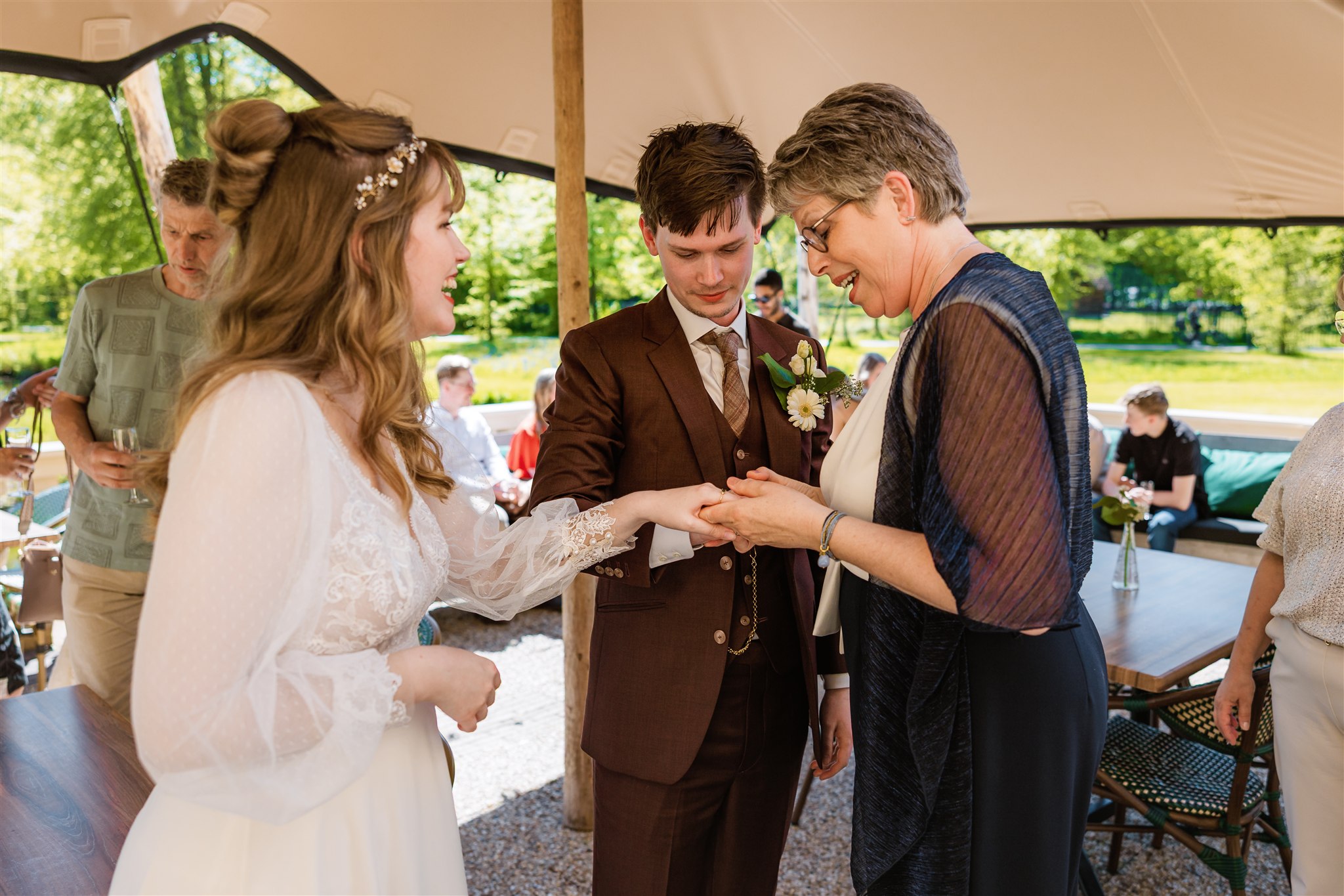 De moeder van de bruid bewondert de ring van de bruid terwijl de bruidegom ernaast staat op een trouwreceptie in de open lucht.