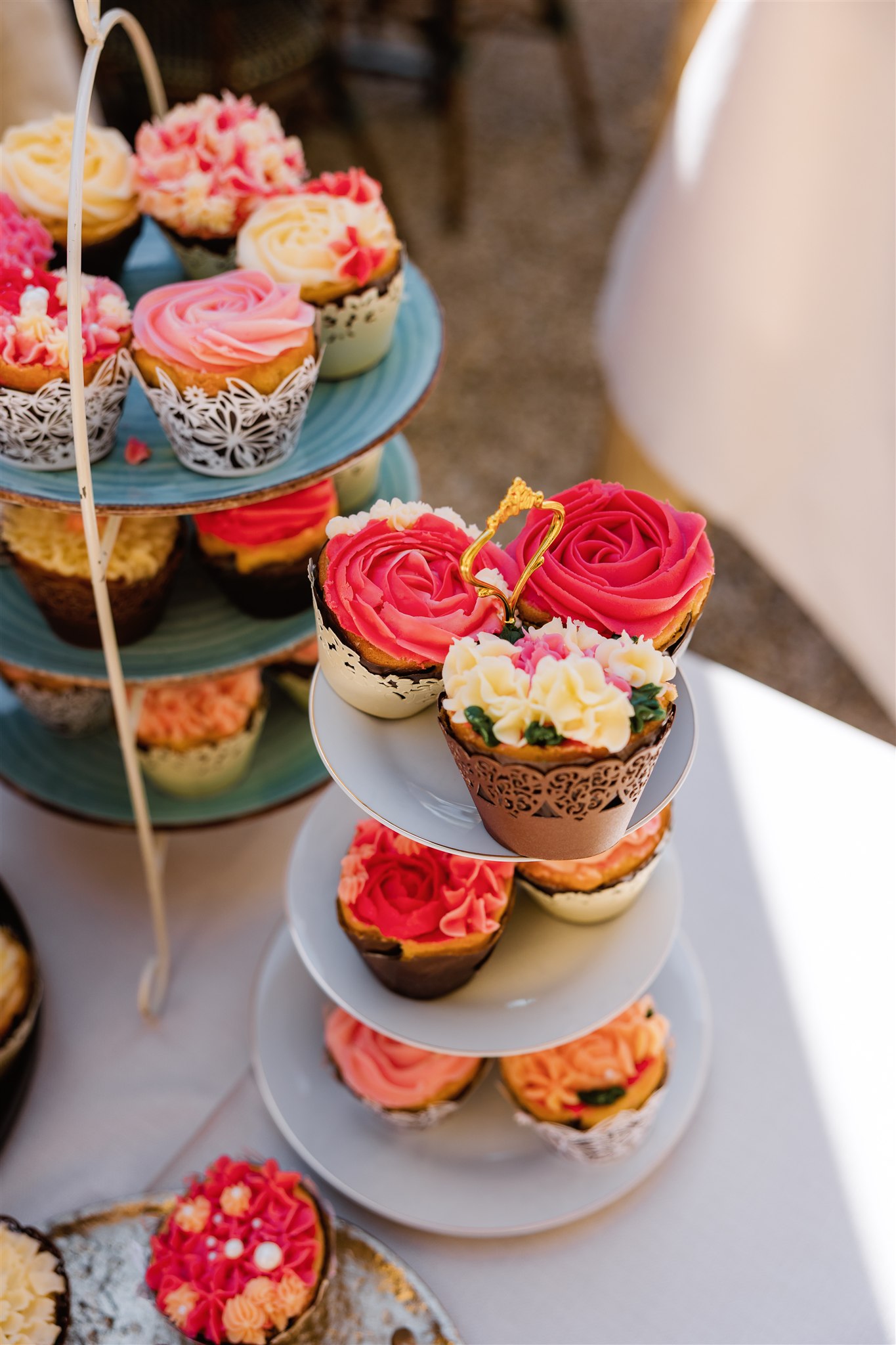 Cupcakes met roosvormig glazuur in roze, rode en crèmekleuren, uitgestald op trapsgewijs geplaatste standaards.