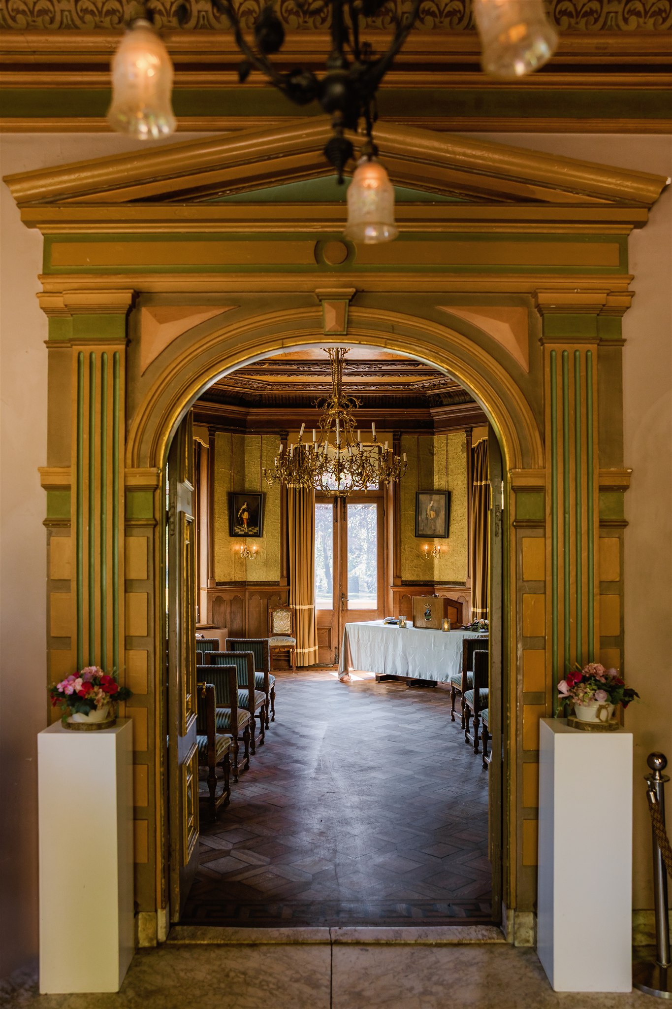 Sierlijke boogdoorgang die leidt naar de elegante Ridderzaal met kroonluchters, stoelen en een tafel met wit tafelkleed.