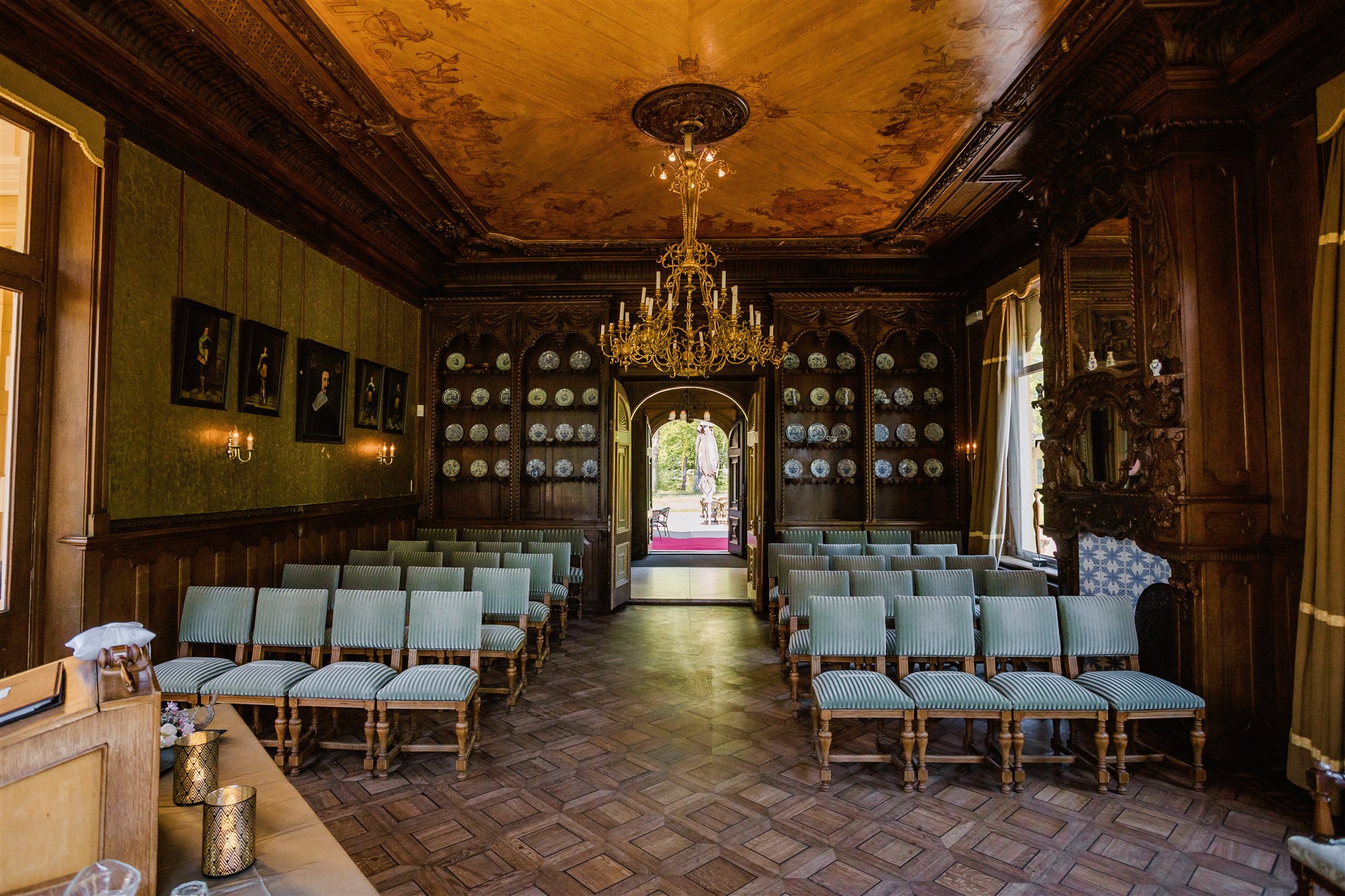 De Ridderzaal van Borg Nienoord met houtsnijwerk, blauwe stoelen en kroonluchter.