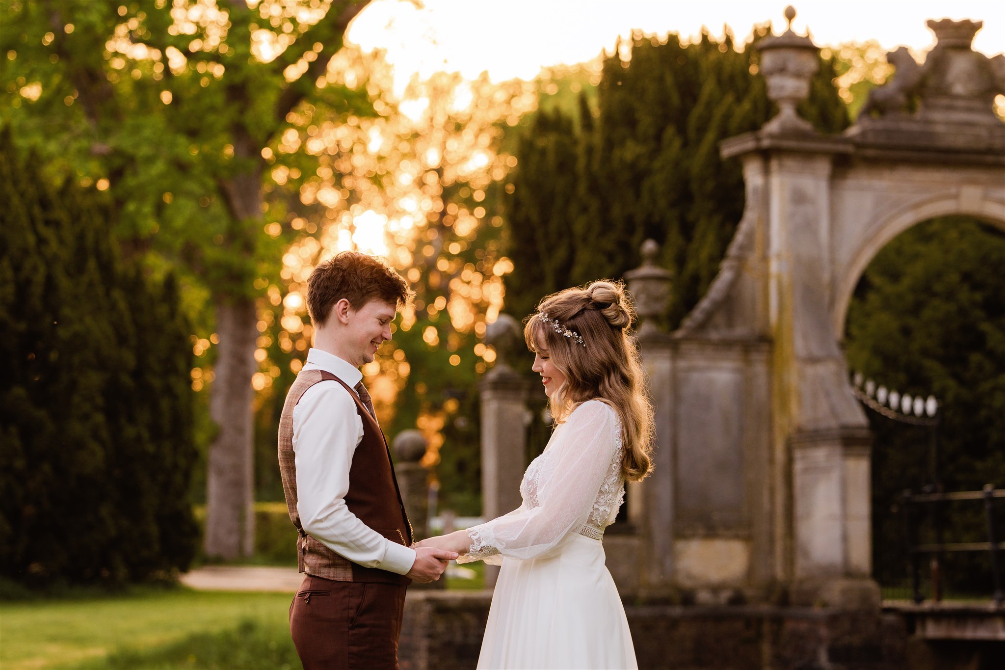 Een bruidspaar houdt elkaars hand vast bij zonsondergang voor de toegangspoort van Borg Nienoord.