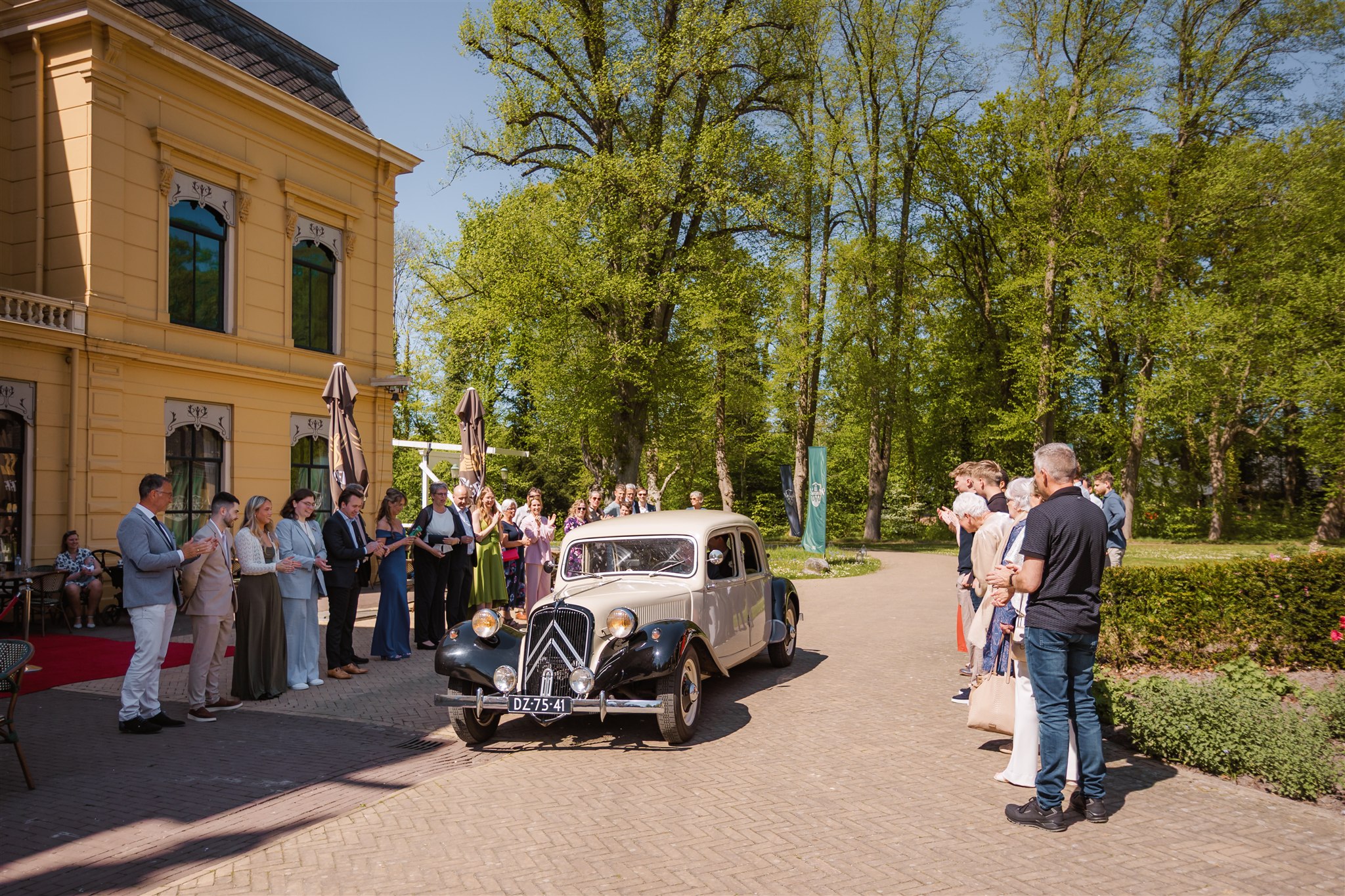 Een oldtimer met bruidspaar arriveert tussen de erehaag van daggasten.