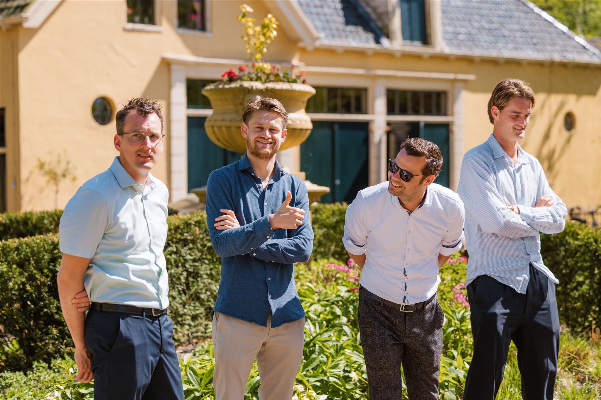 Vier mannen daggasten van een bruiloft staan lachend en kletsend op een zonnige dag te wachten op het bruidspaar.