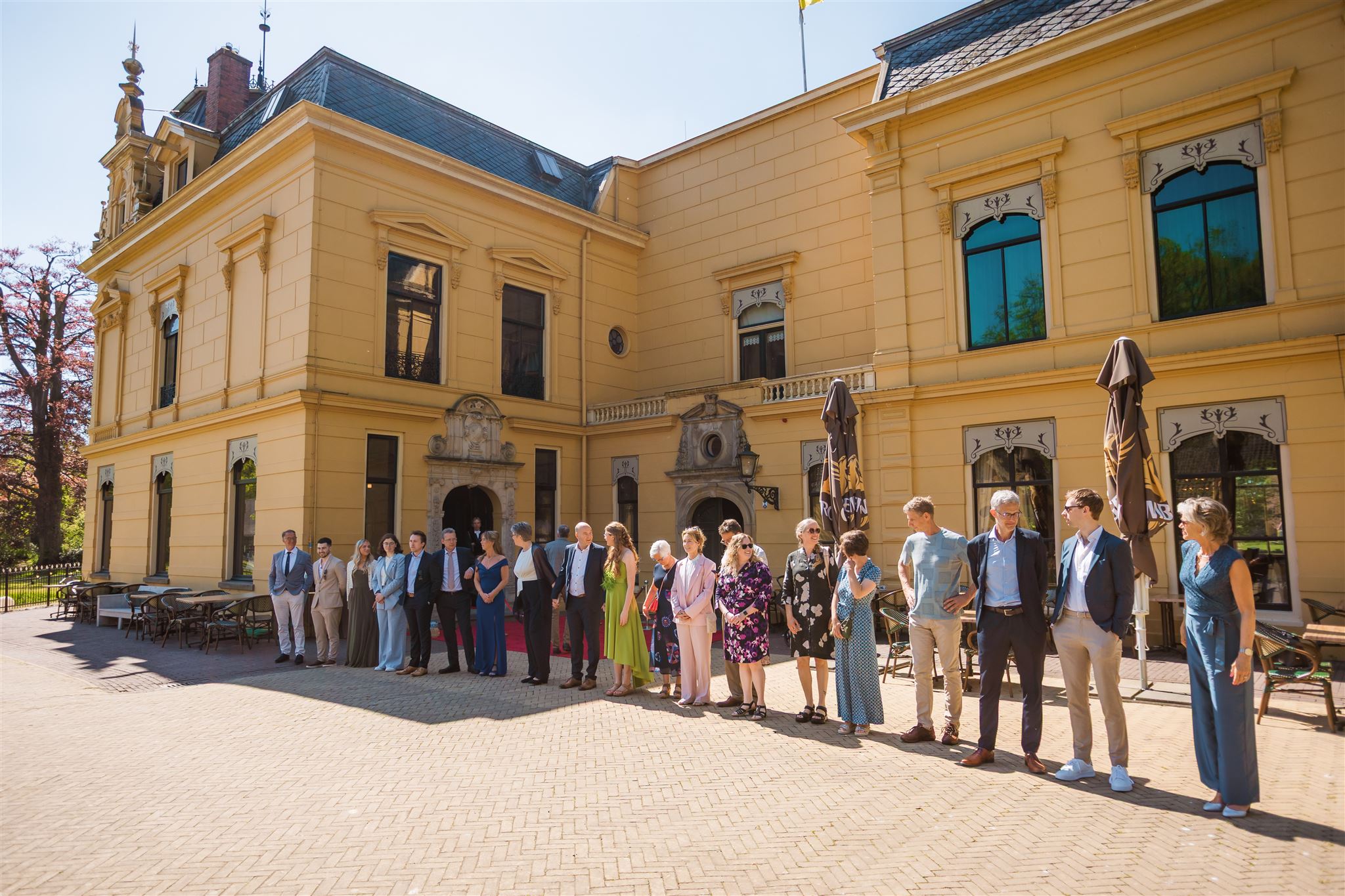 Een groep rij daggasten staat voor het gebouw van Landgoed Nienoord te wachten op het bruidspaar.