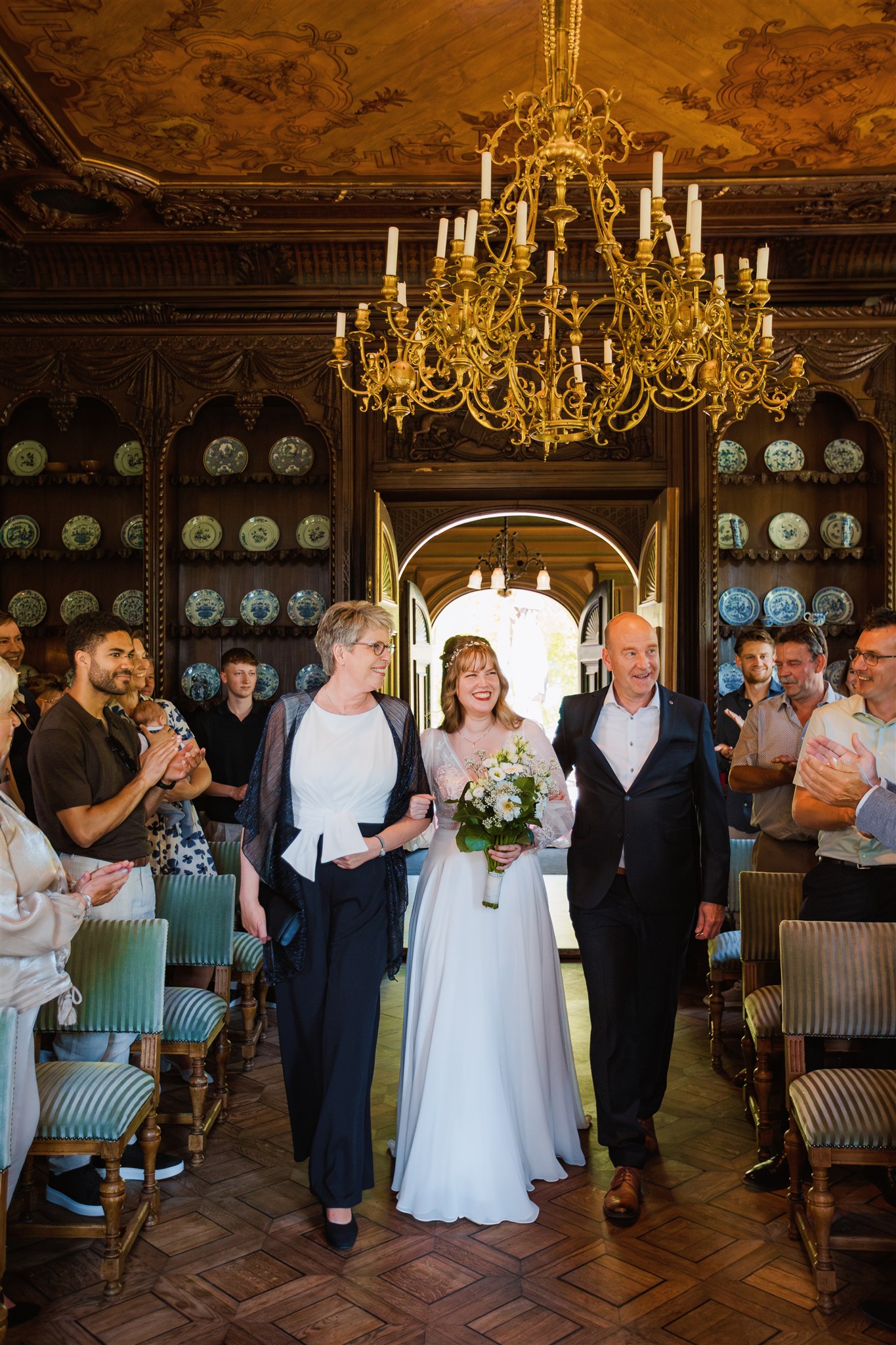 Bruid loopt met haar ouders door de Ridderzaal van Borg Nienoord tijdens haar trouwceremonie