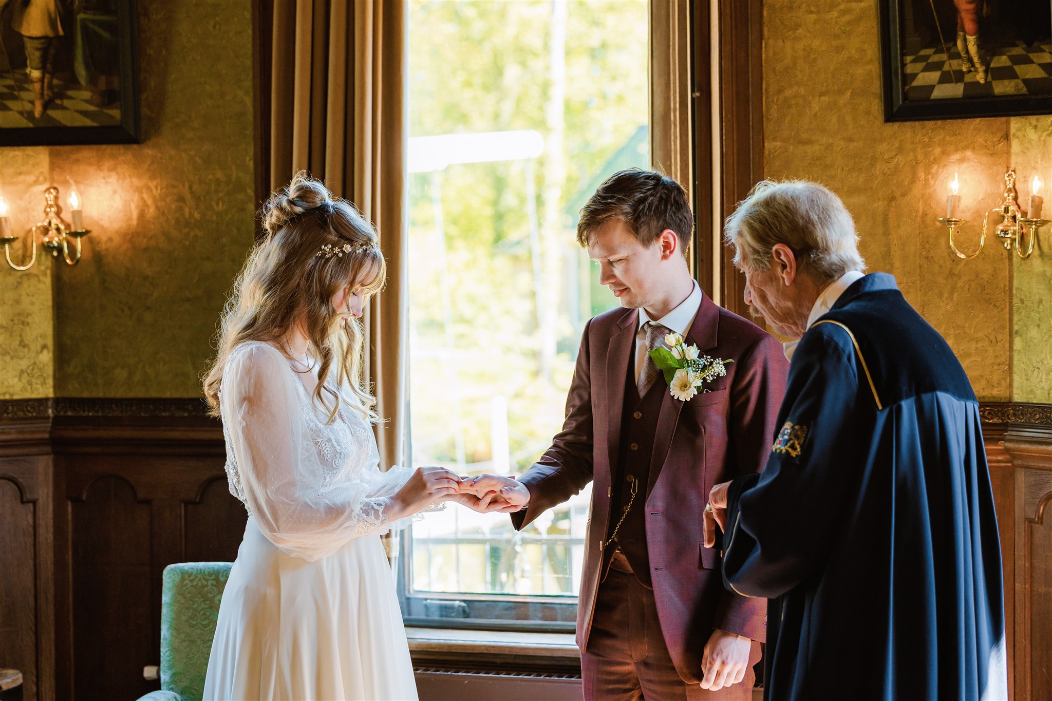 Bruid en bruidegom wisselen ringen uit tijdens hun huwelijksceremonie bij Borg Nienoord, waarbij de trouwambtenaar naast hen staat.