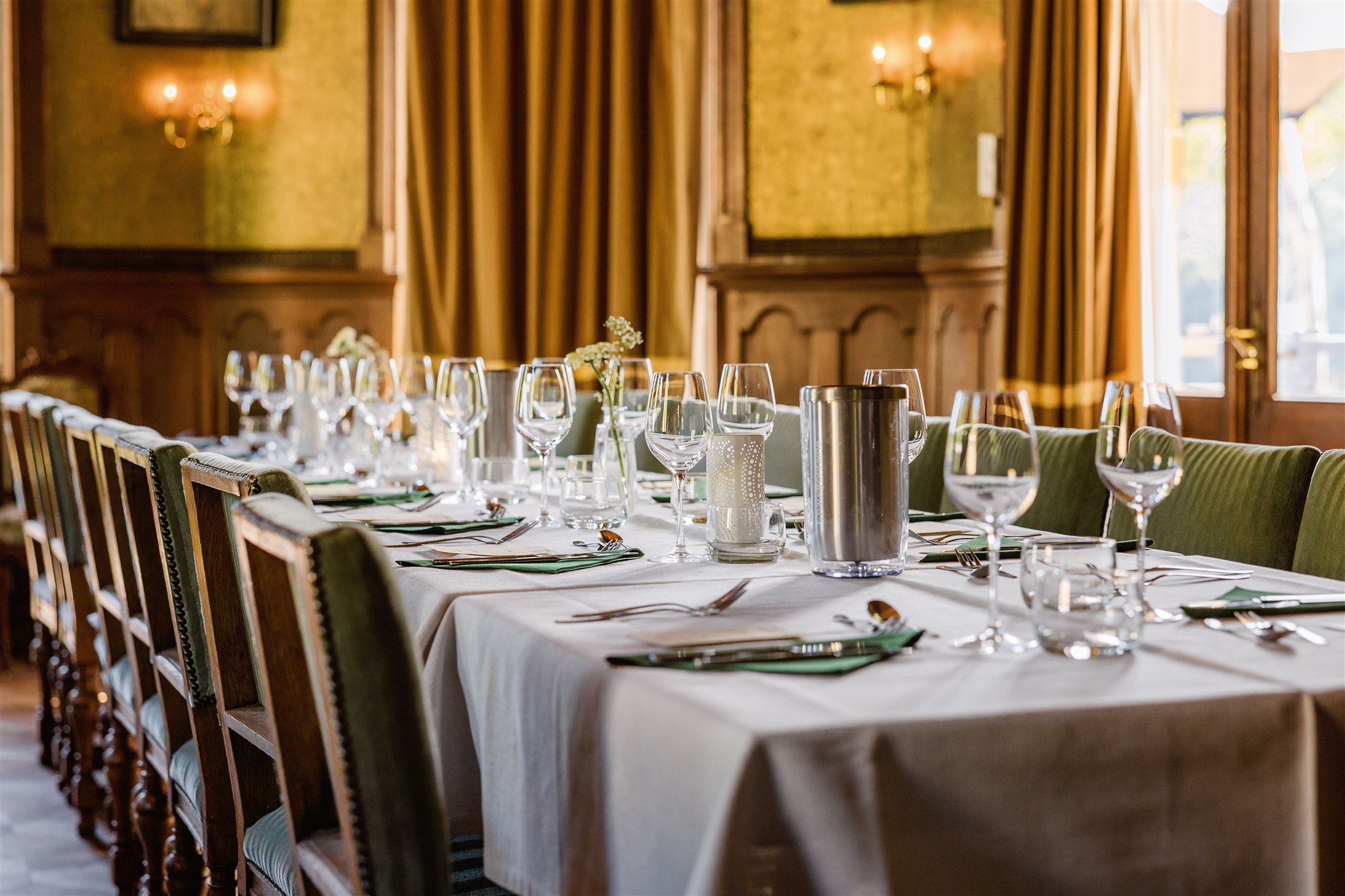 Elegante eettafel gedekt met glaswerk en bestek in een warm verlichte, chique eetzaal met gouden gordijnen.