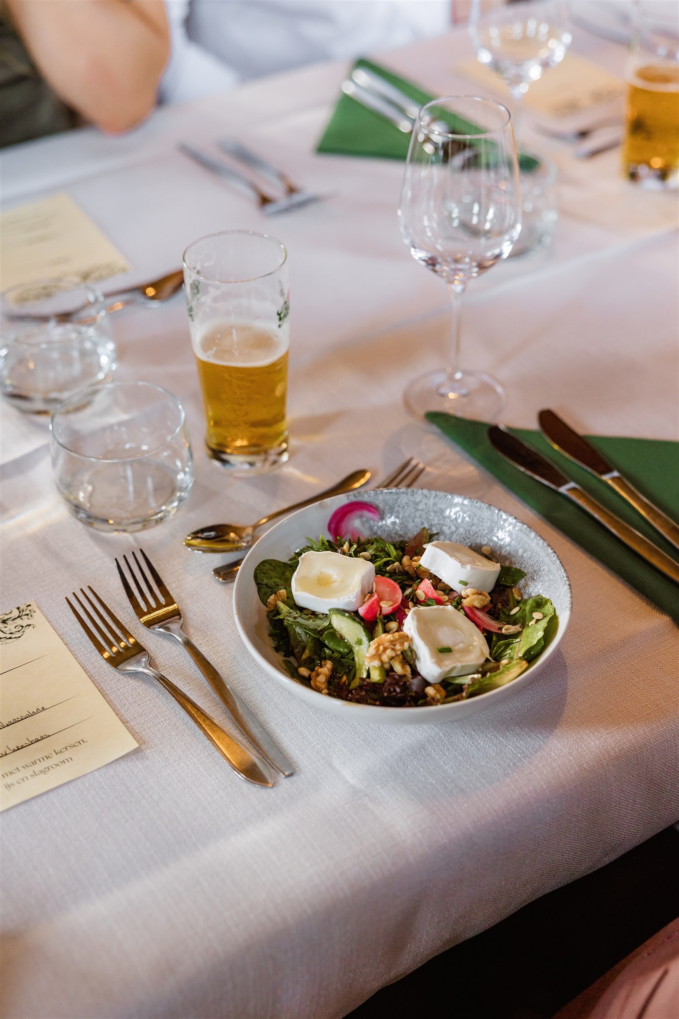 Een salade met geitenkaas, noten en groenten op een gedekte eettafel met een glas bier.