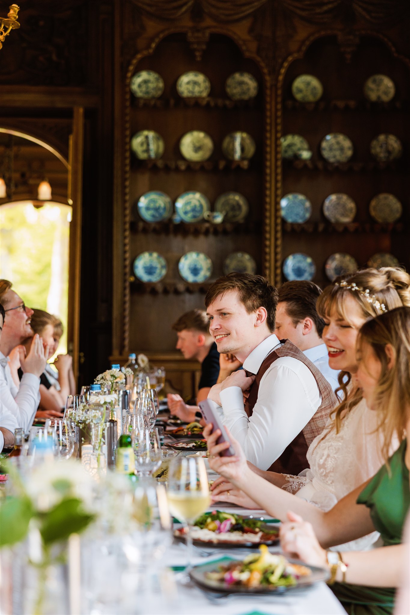 Mensen zitten rond een gedekte tafel, glimlachen en genieten van een maaltijd in een elegante kamer met blauwe decoratieve borden.