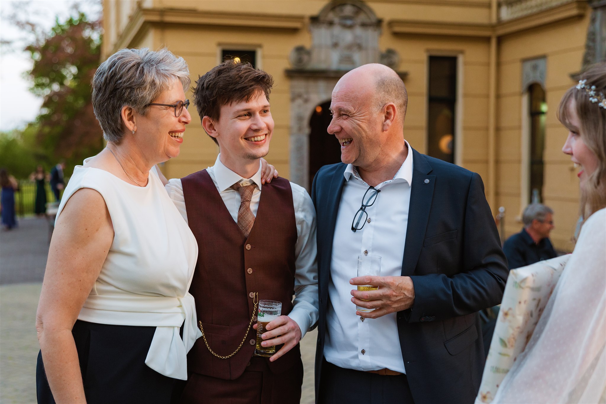 Bruidegom wordt buiten omhelsd door zijn lachende schoonouders.