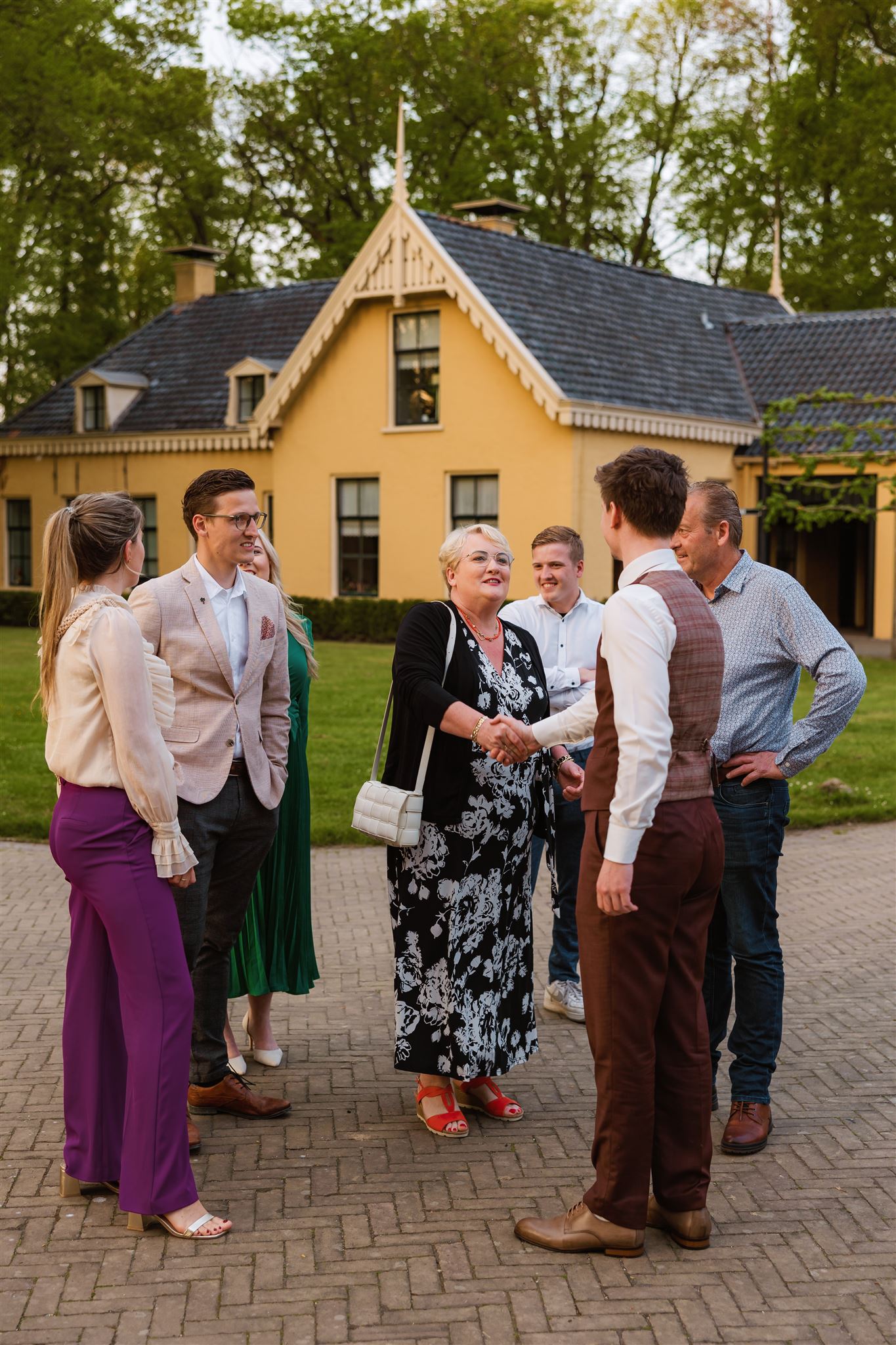 De bruidegom ontvangt buiten de avondgasten en schudt hen de hand.