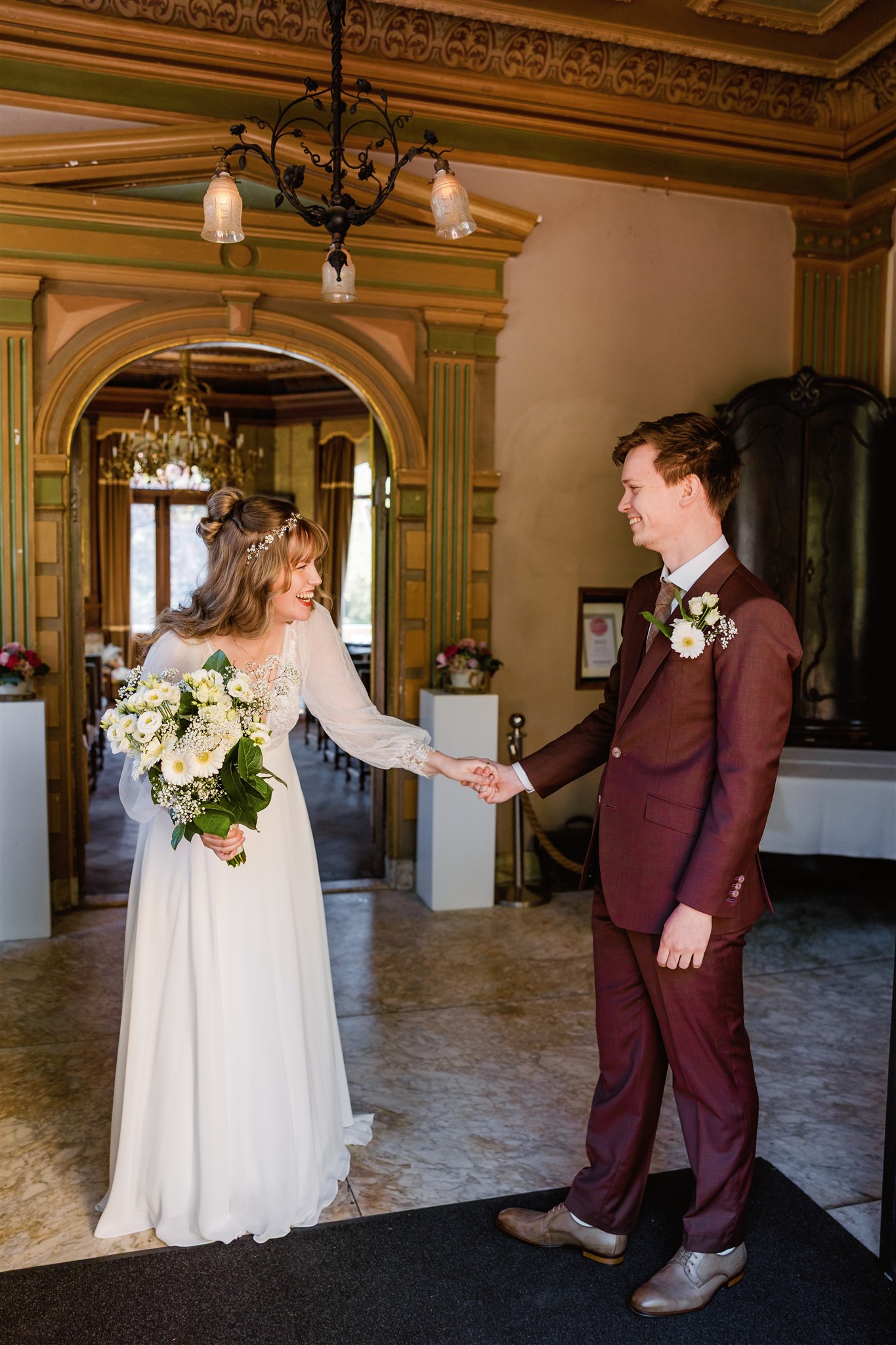 Bruid en bruidegom glimlachen naar elkaar en houden elkaars hand vast, verrast over hoe mooi ze eruitzien.