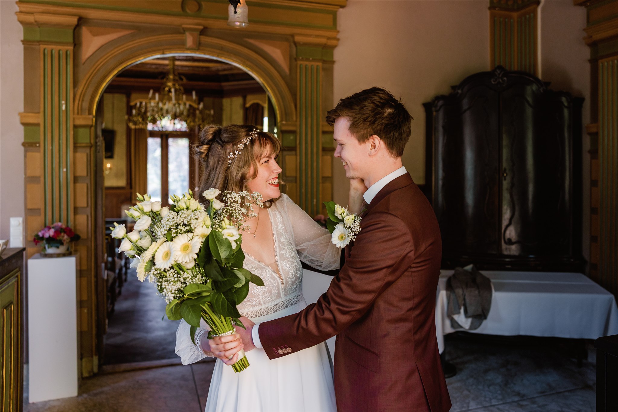 Een bruid met een boeket in haar hand lacht naar haar bruidegom tijdens hun first look.