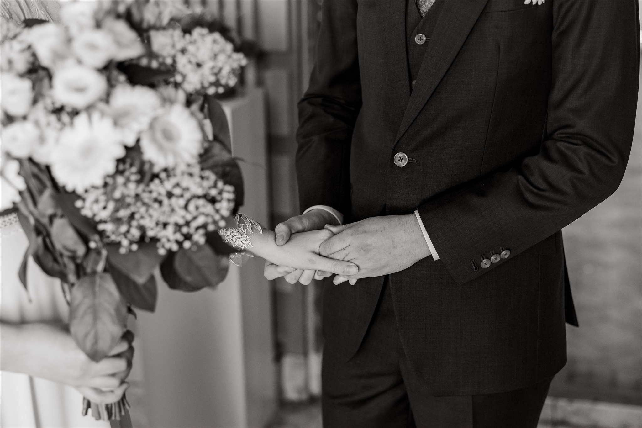 Een bruidegom houdt voorzichtig de hand van de bruid vast terwijl zij een boeket bloemen vasthoudt, op een zwart-wit foto.