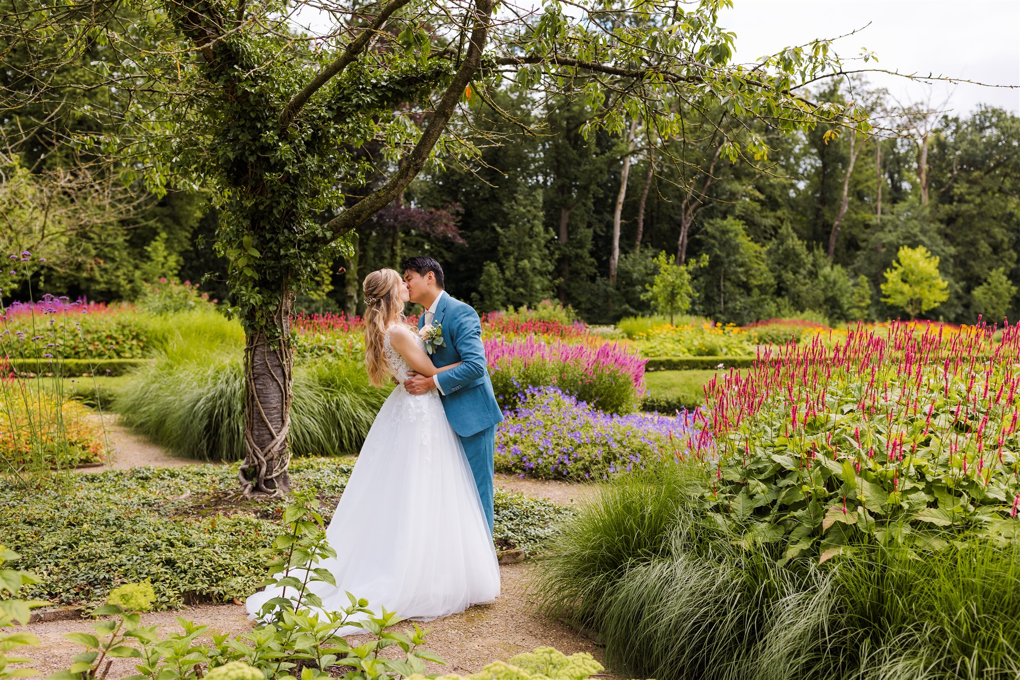 Bruidspaar kust elkaar in de bloeiende Engelse tuin van trouwlocatie Borg Nienoord