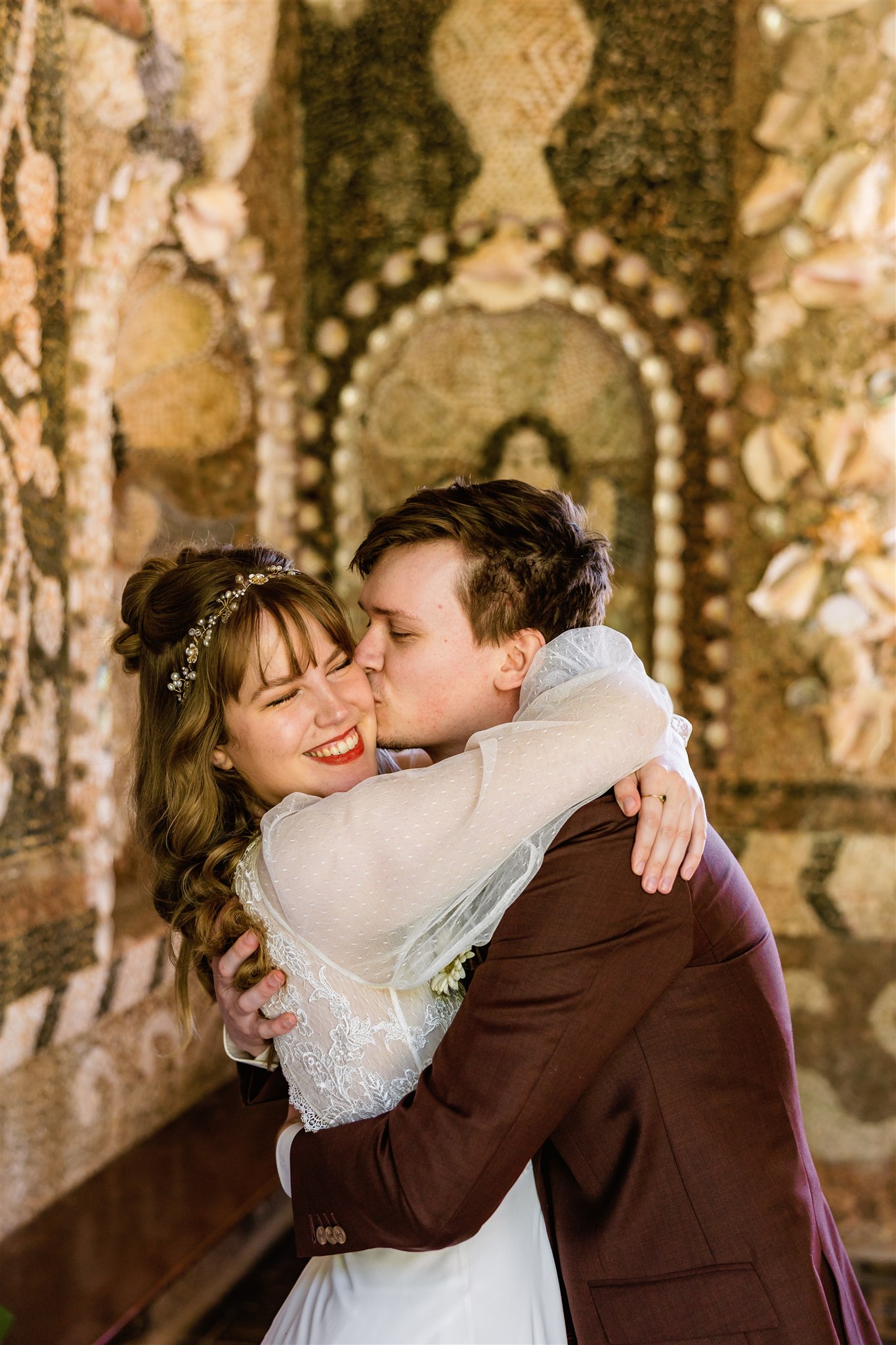 Bruidegom kust zijn bruid op de wang in de Schelpengrot op Landgoed Nienoord.