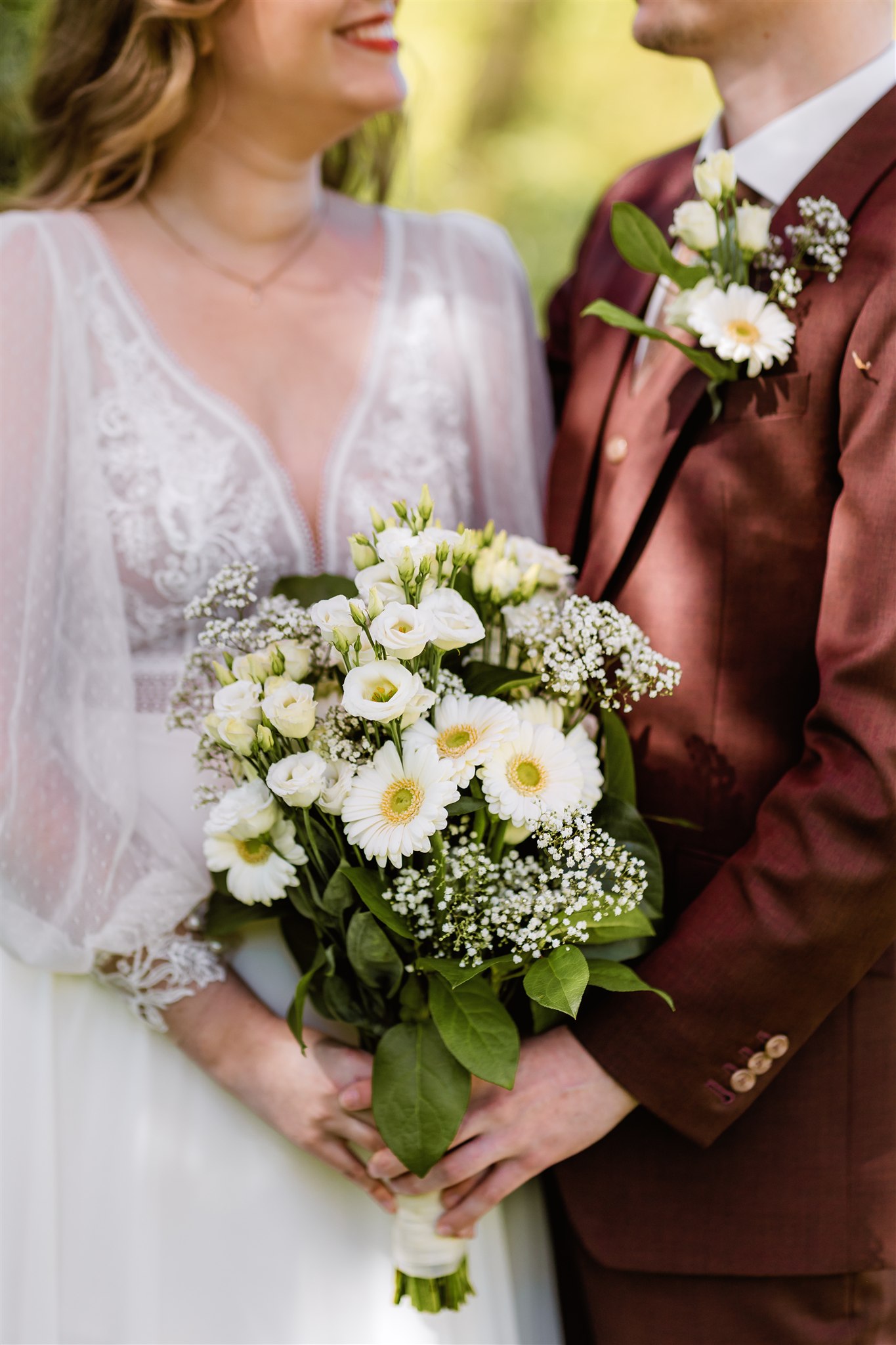 Bruid en bruidegom houden een trouwboeket met witte bloemen vast en glimlachen naar elkaar op hun trouwdag.