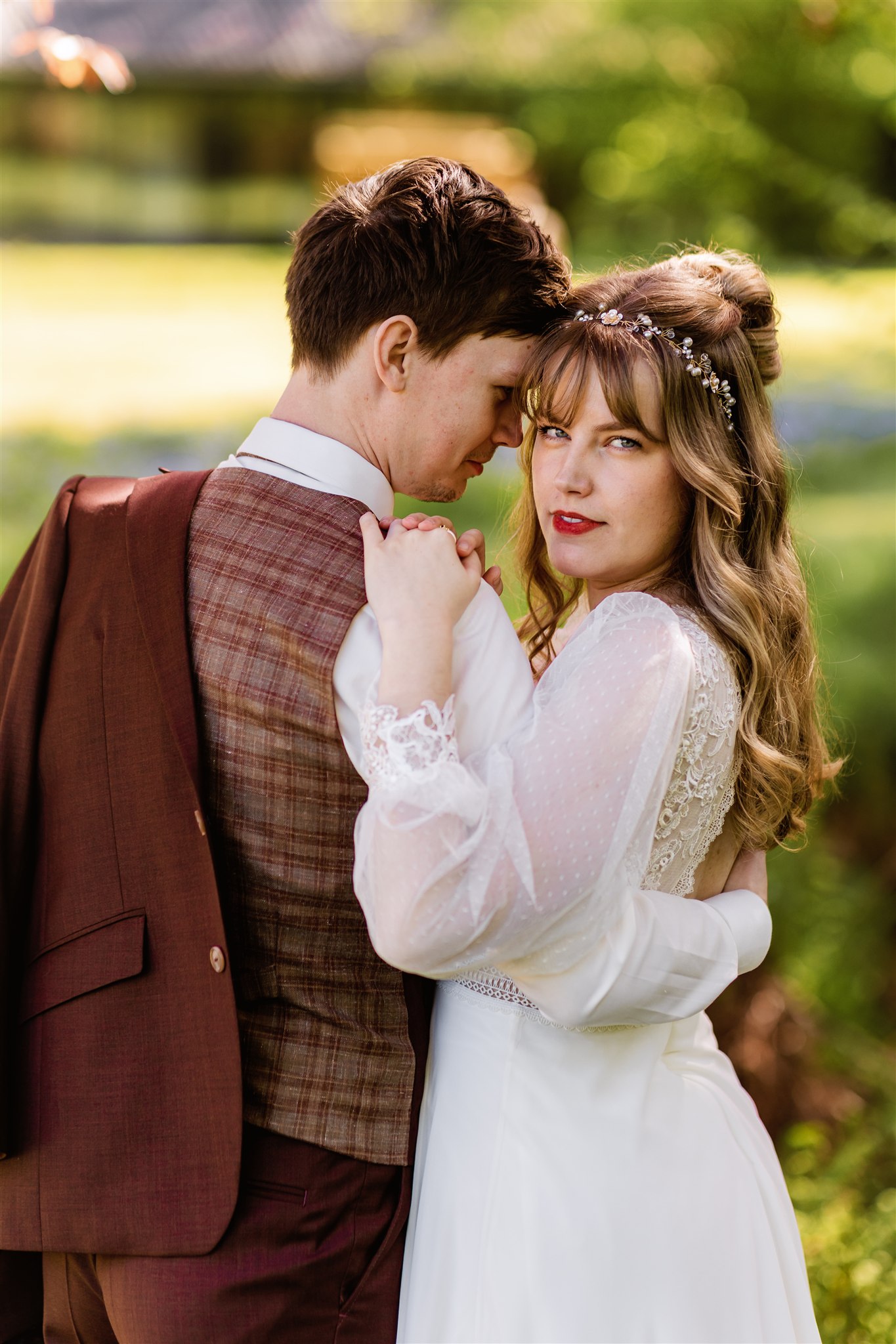 Een bruid en bruidegom omhelzen elkaar buiten; de bruid kijkt naar de camera terwijl de bruidegom naar haar kijkt.