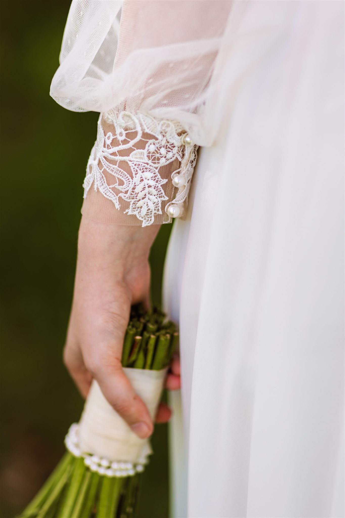 Kanten details en parelknoopjes van de mouwen van een trouwjurk.