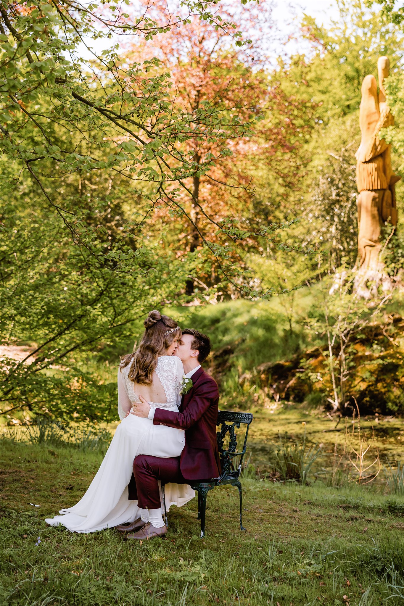 Een bruid zit op de schoot van een bruidegom terwijl ze kussen op een stoel in de tuin op Landgoed Nienoord.