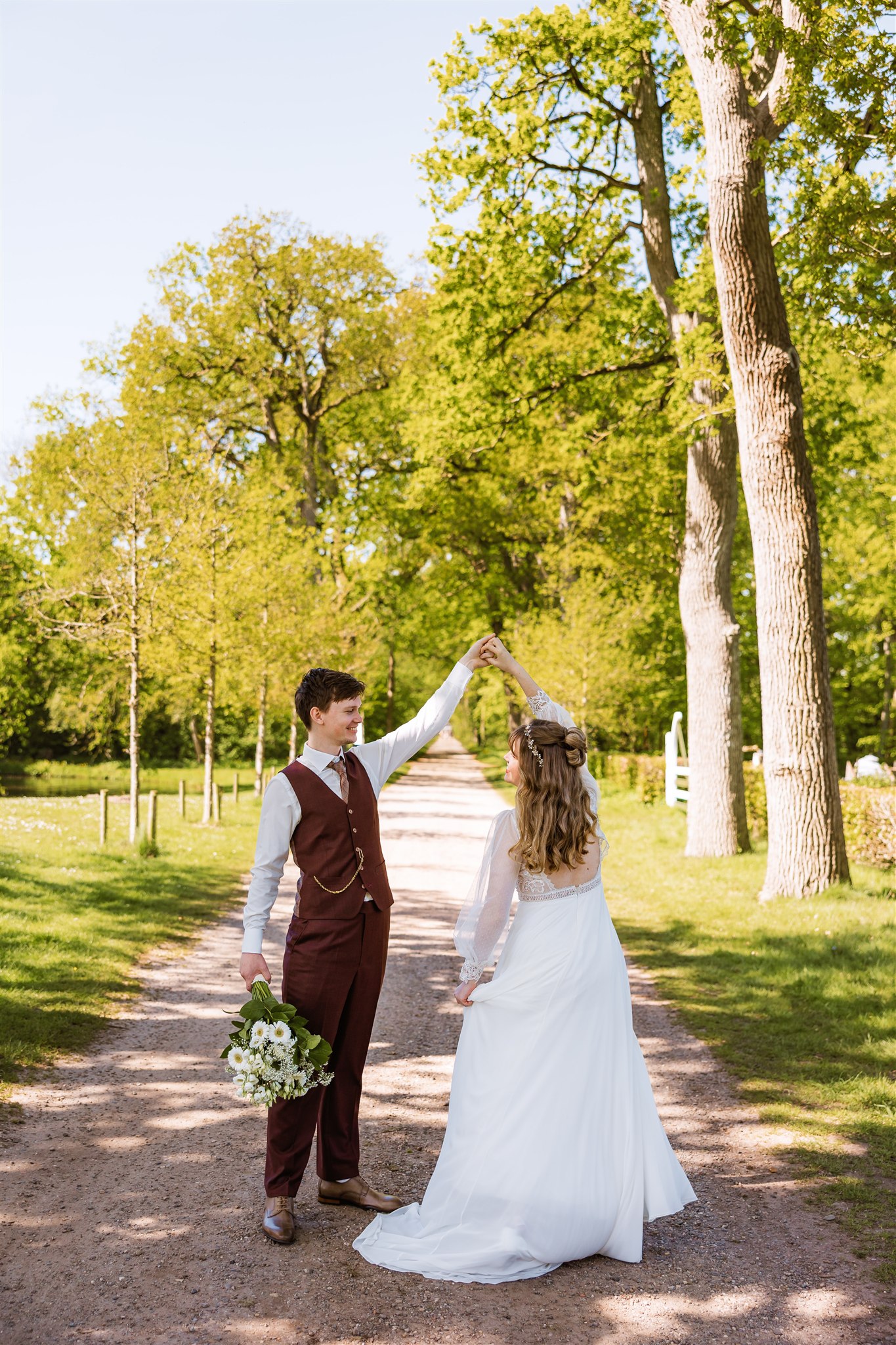 Bruid en bruidegom dansen buiten op een zonnig bospad op Landgoed Nienoord.