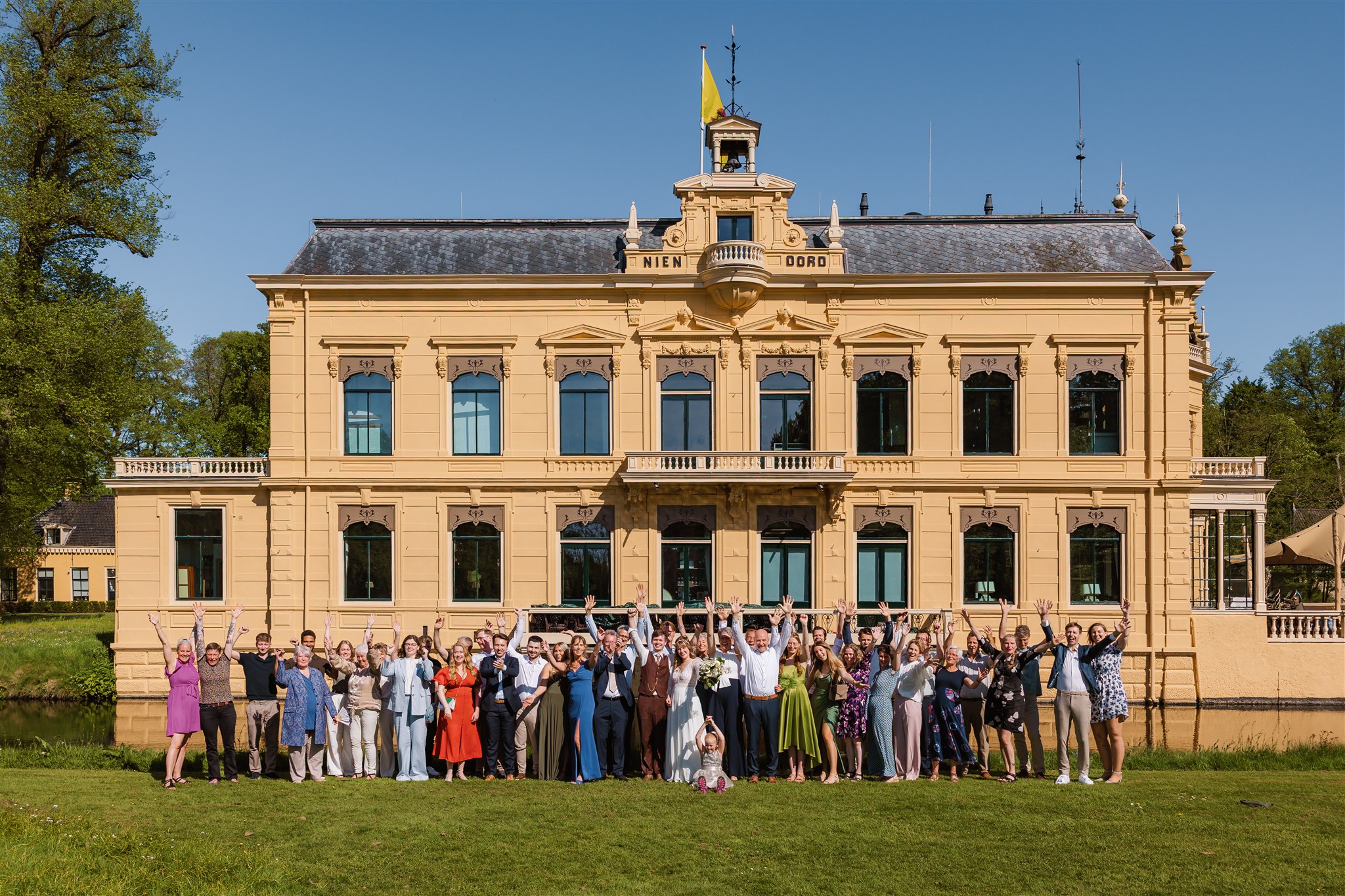 De hele groep daggasten juicht op een groepsfoto voor het gebouw van Borg Nienoord.