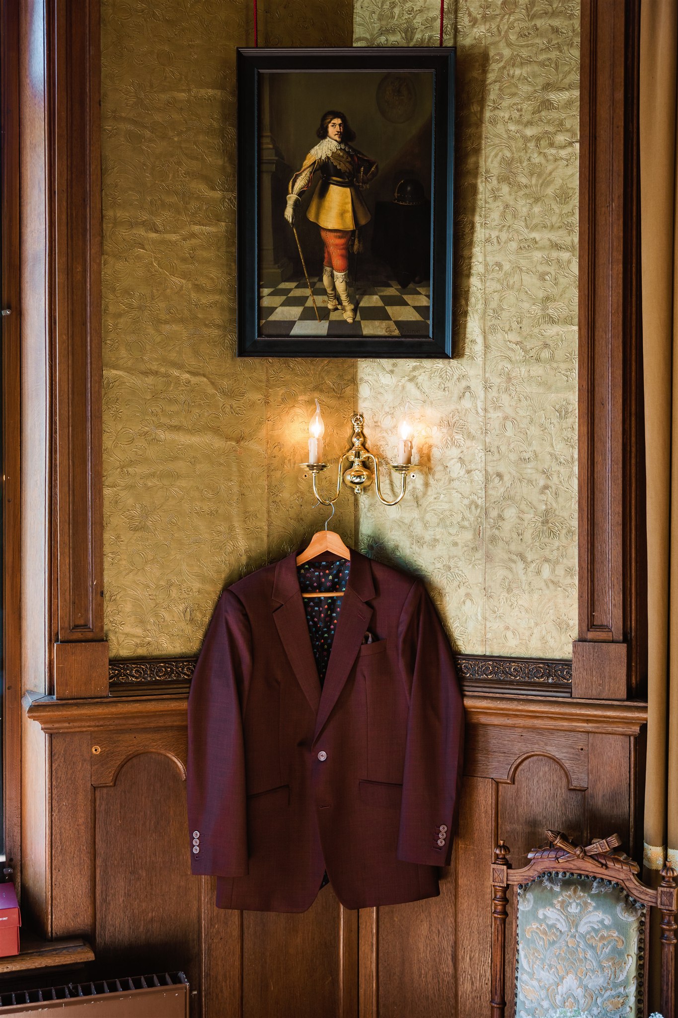 Een bordeauxrood trouwcolbert hangt onder een ingelijst schilderij.