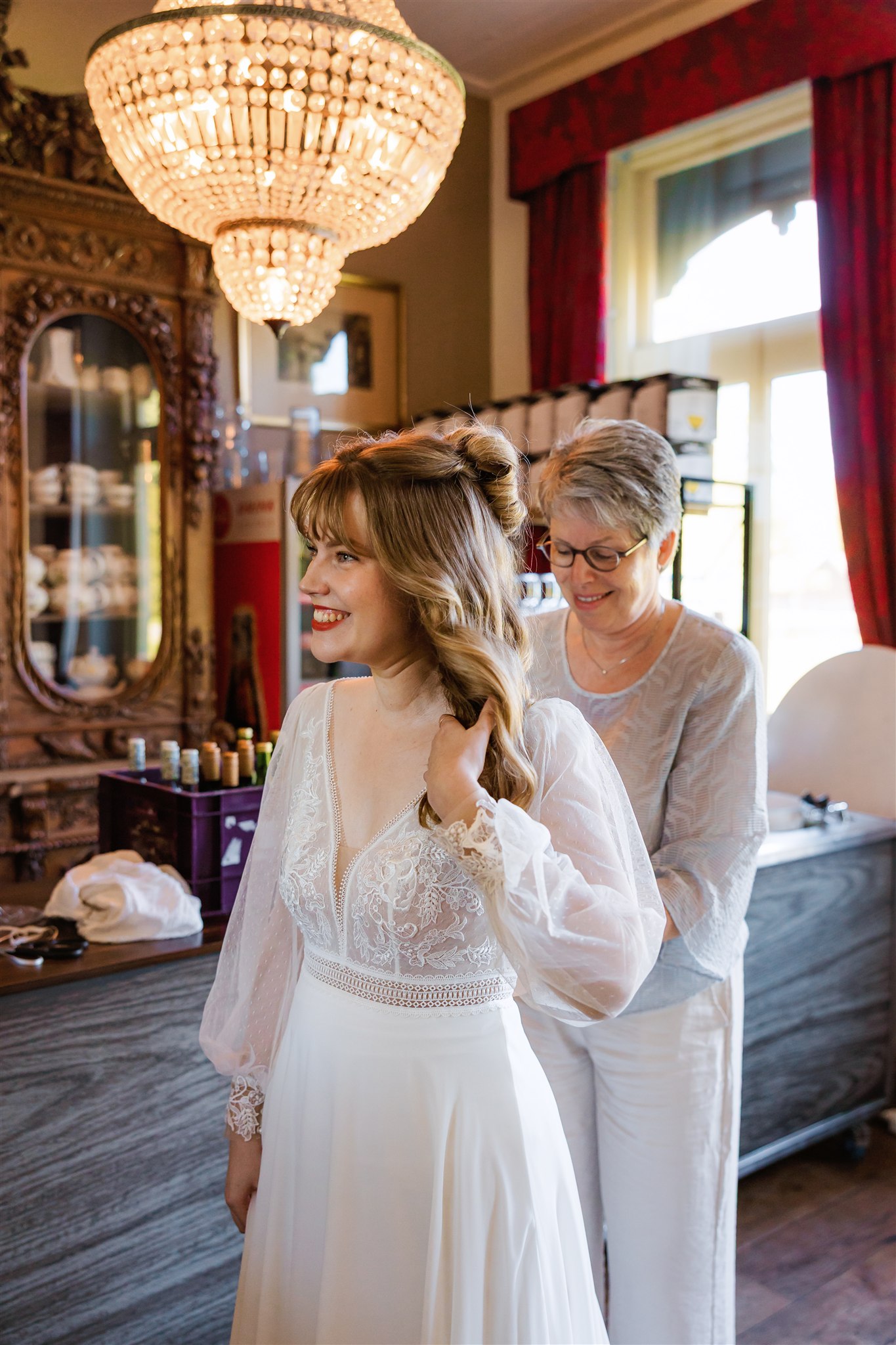 Bruid glimlacht terwijl haar moeder haar trouwjurk dichtritst.