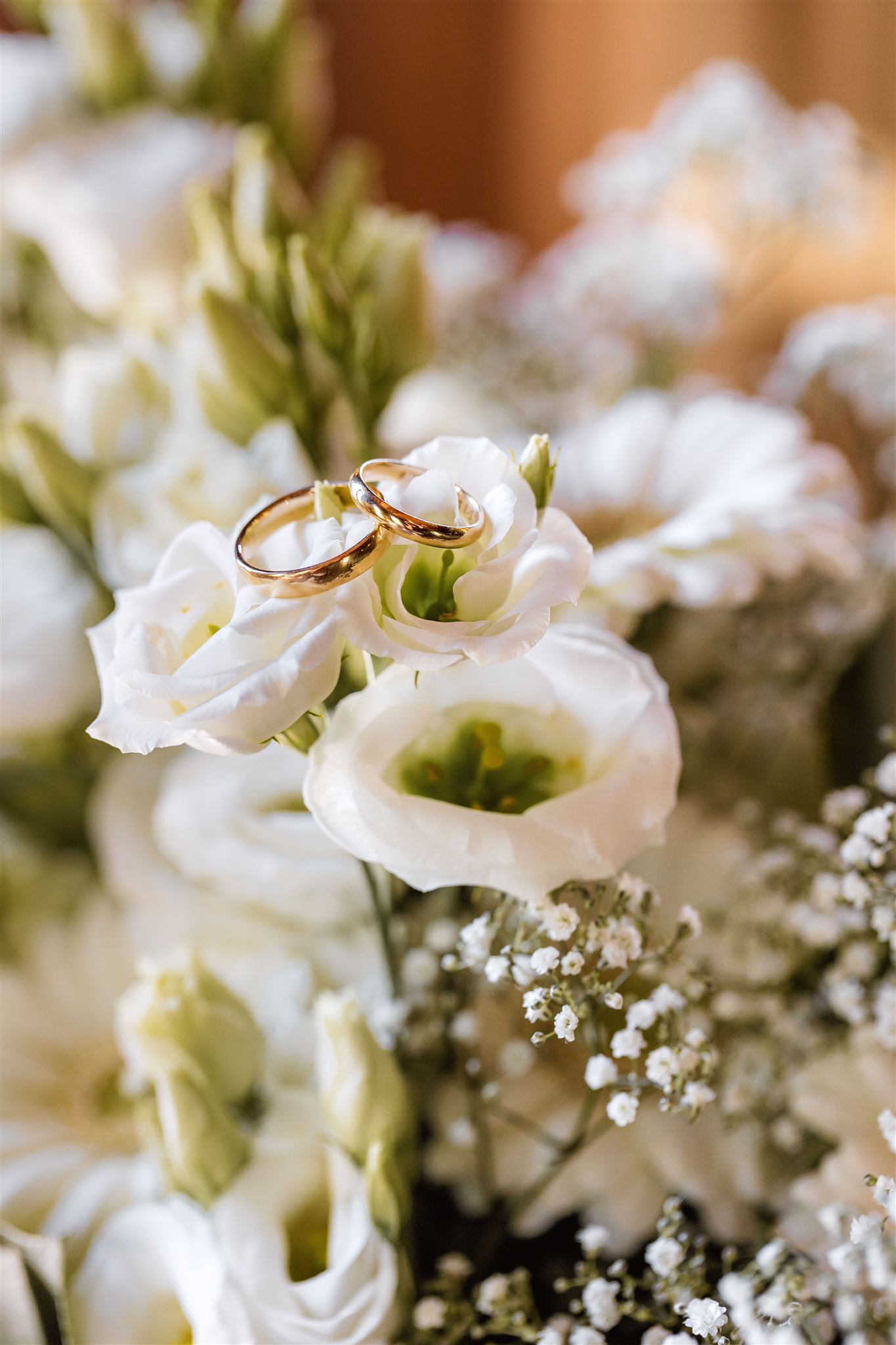 Twee gouden trouwringen rustend op witte bloemen met gipskruid op de achtergrond.