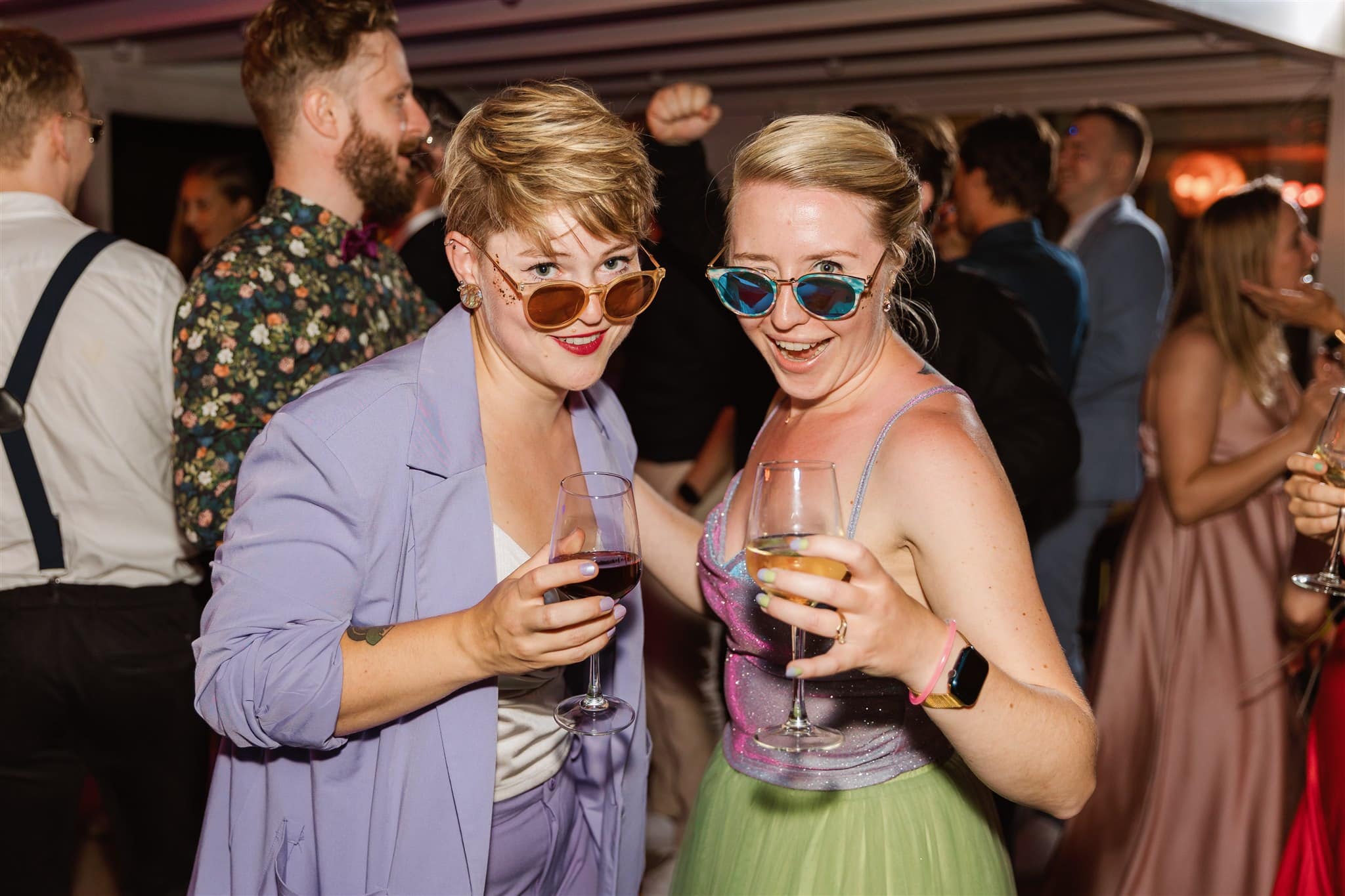 Twee vrouwen met zonnebrillen lachen en houden drankjes vast op een trouwfeest bij de Paalkoepel.
