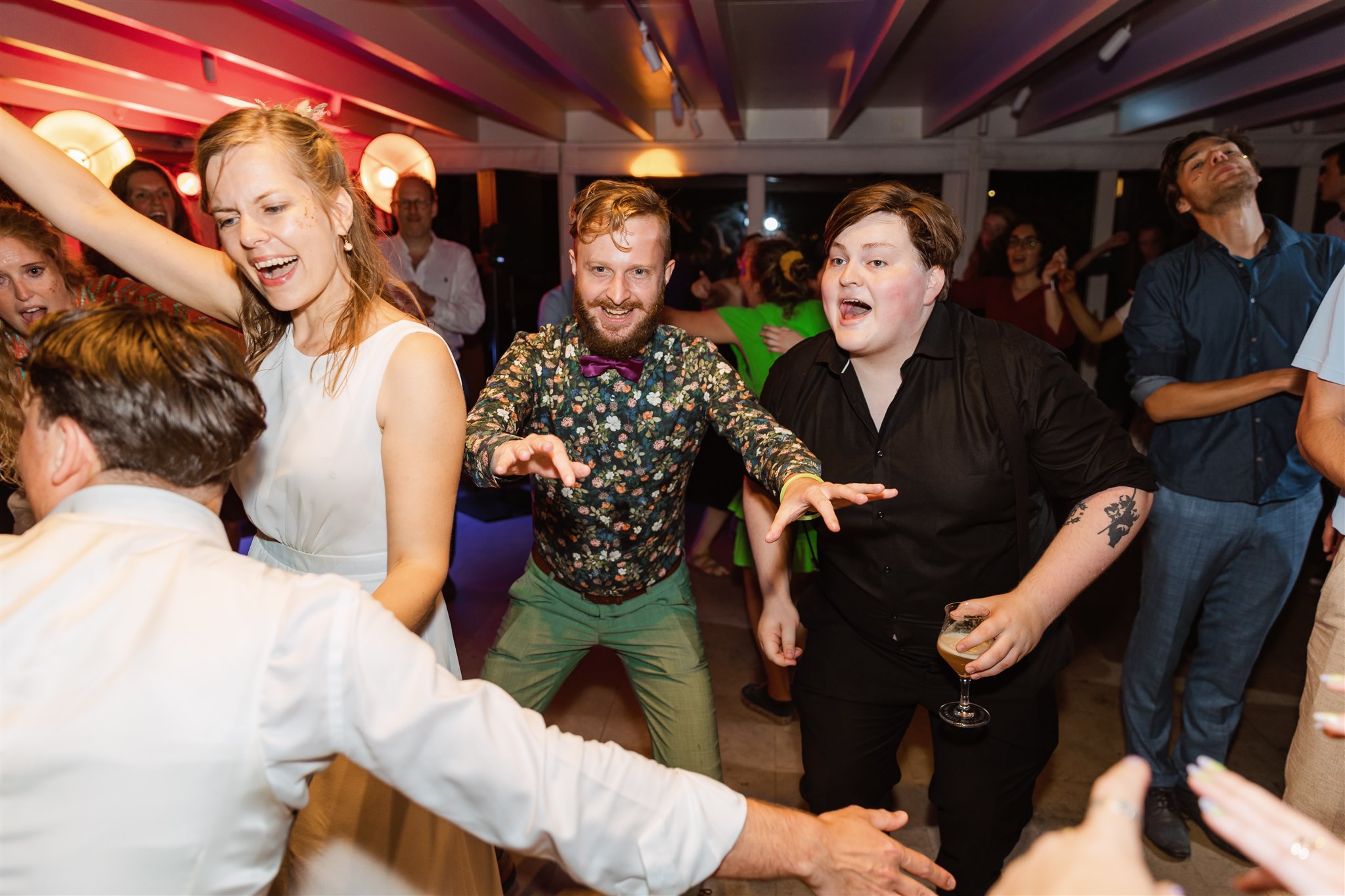 Mensen dansen energiek op een levendig binnenfeest, glimlachen en genieten van de muziek onder kleurrijke lampen.