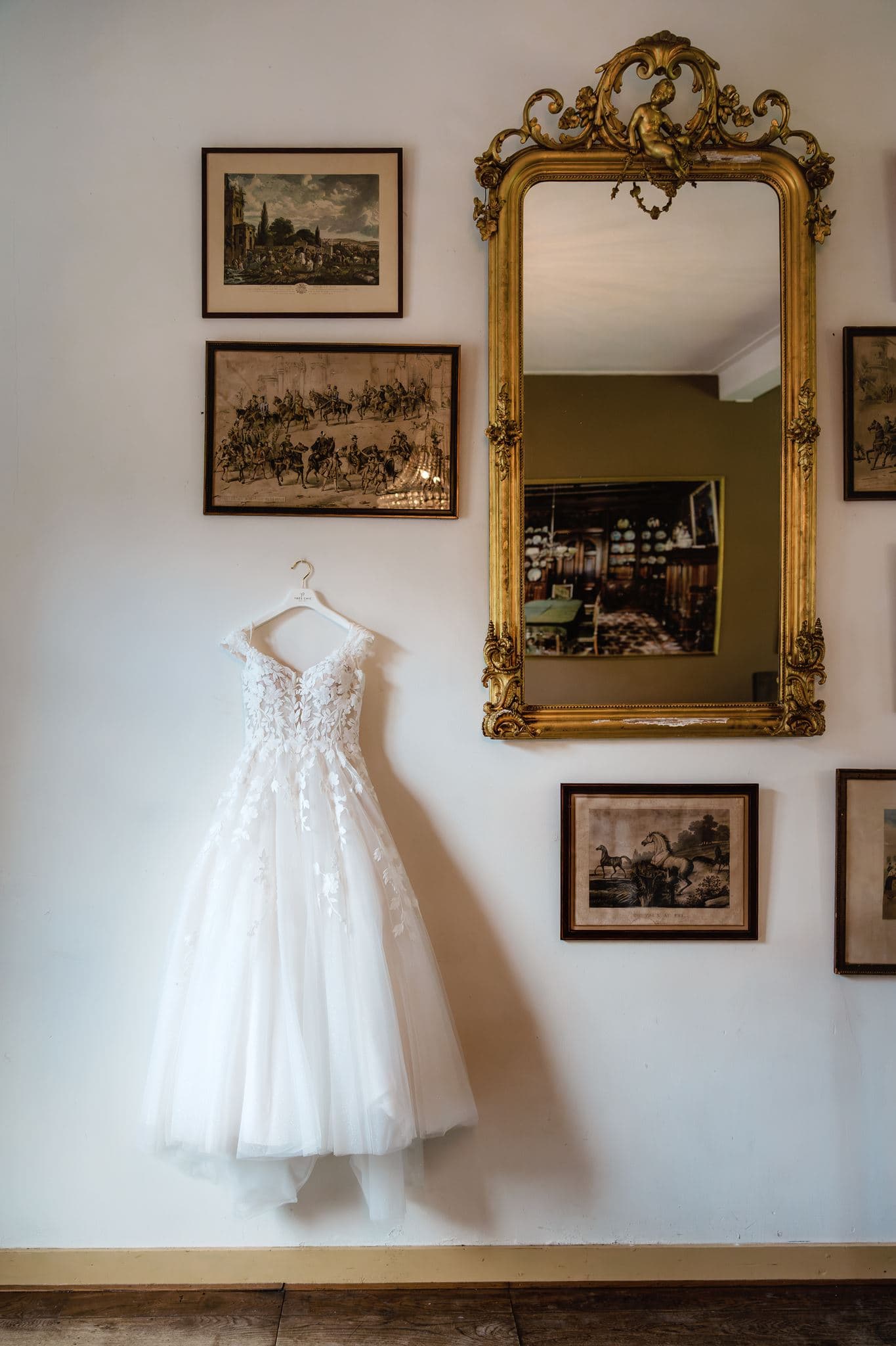 Trouwjurk opgehangen tussen de schilderijen aan de muur van de balzaal van Borg Nienoord.