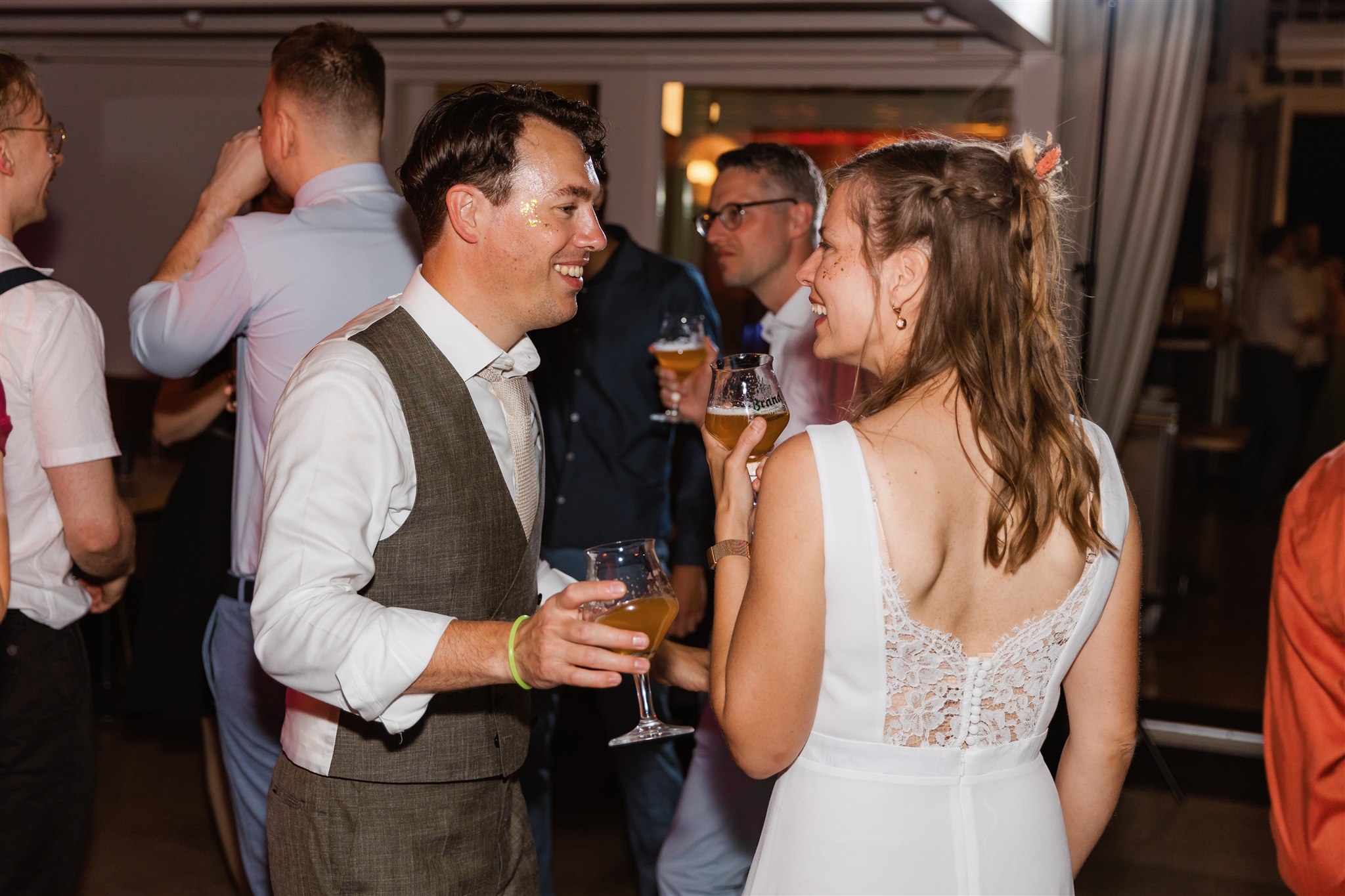 Bruidspaar lacht naar elkaar met een glas bier in de hand tijdens hun trouwfeest bij de Paalkoepel