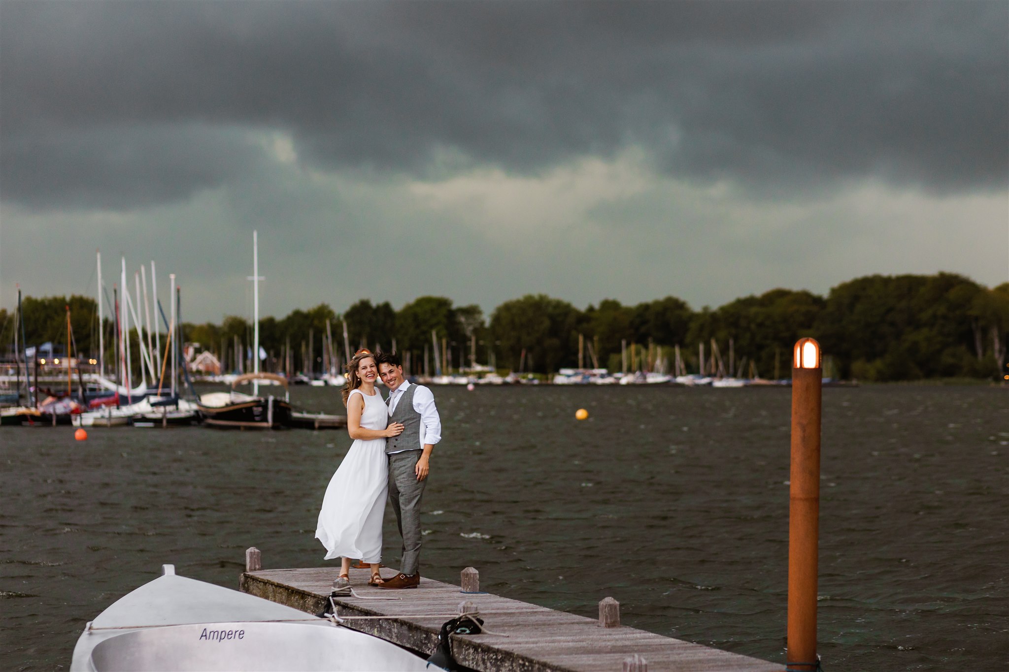 Trouwfoto van een bruidspaar op de steiger van de Paalkoepel onder een stormachtige dreigende lucht