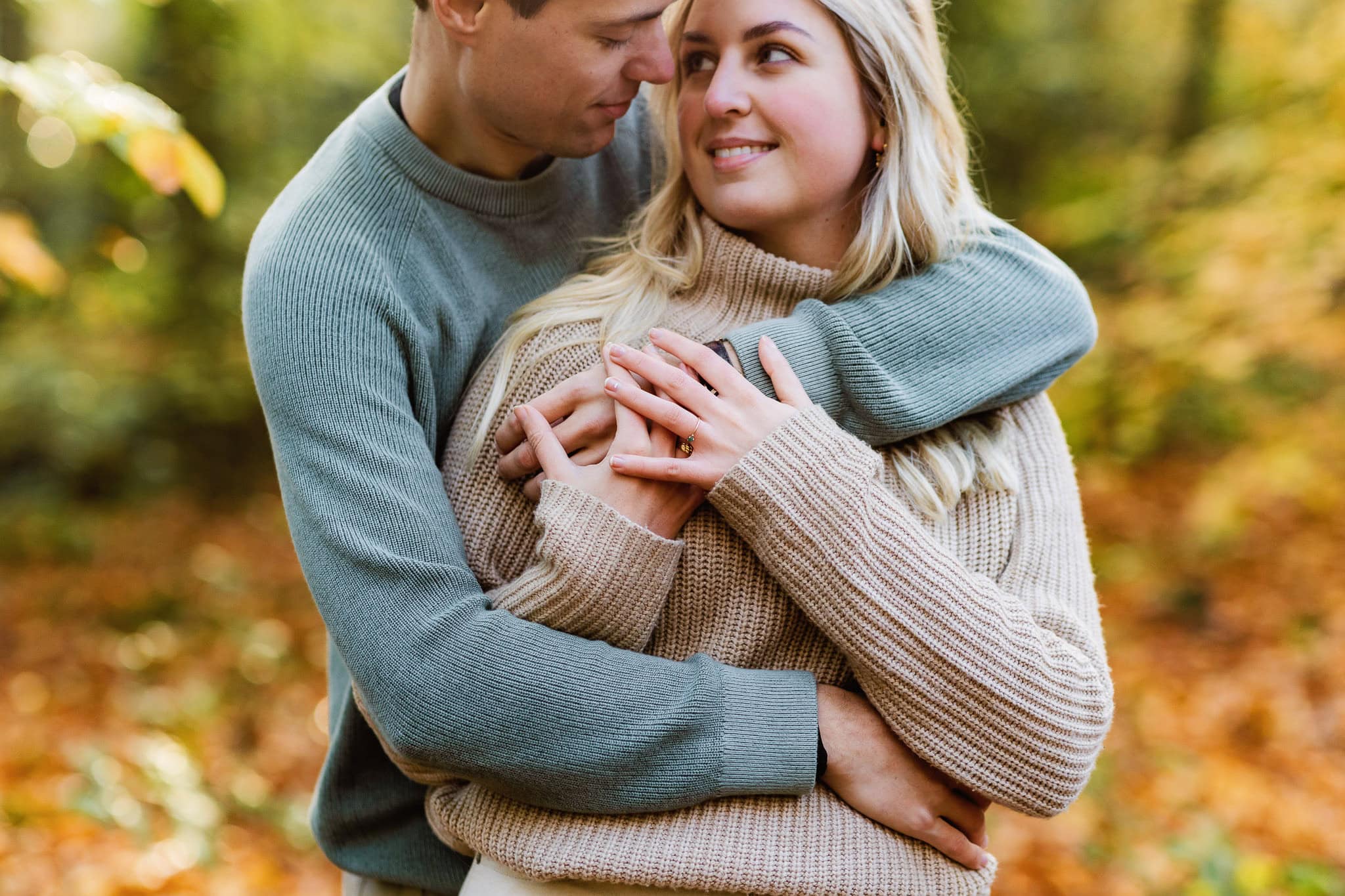 Een stel omhelst elkaar buiten tijdens een loveshoot in Groningen; de vrouw laat een verlovingsring zien terwijl ze naar haar partner lacht.
